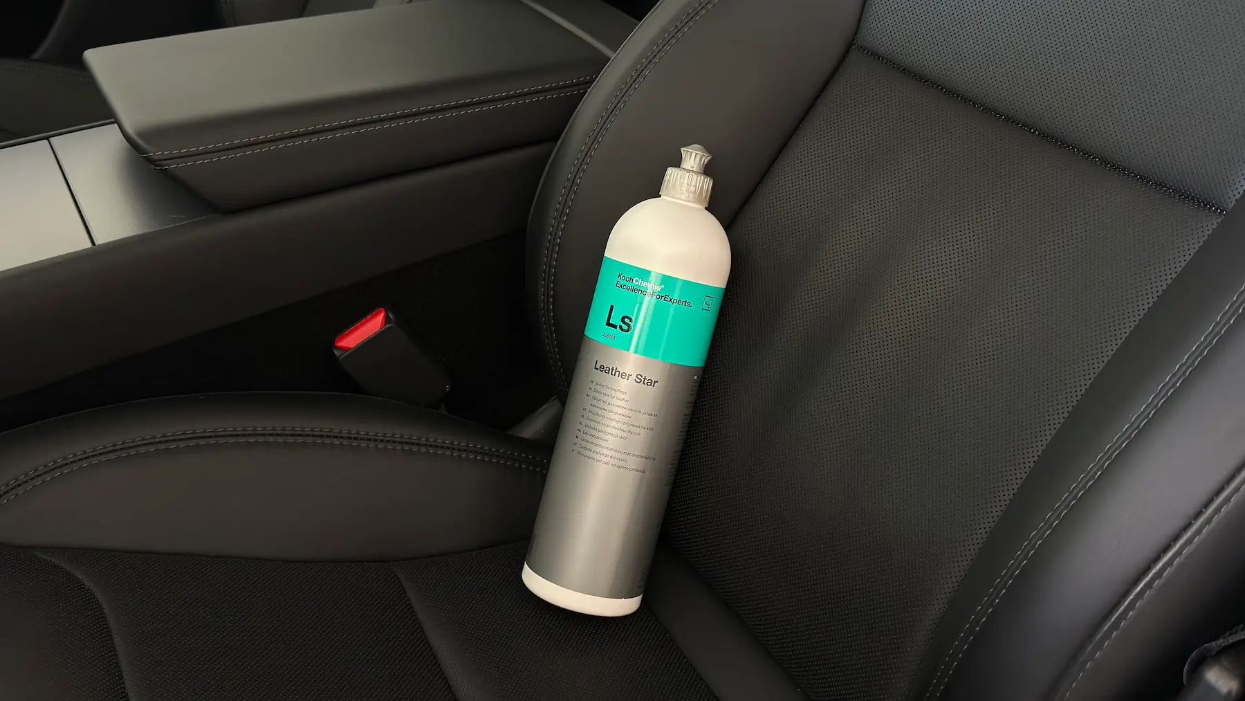 Bouteille de produit Koch Chemie Leather Star posée sur un siège en cuir noir d’une voiture, avec console centrale et boucle de ceinture rouge visibles à côté.