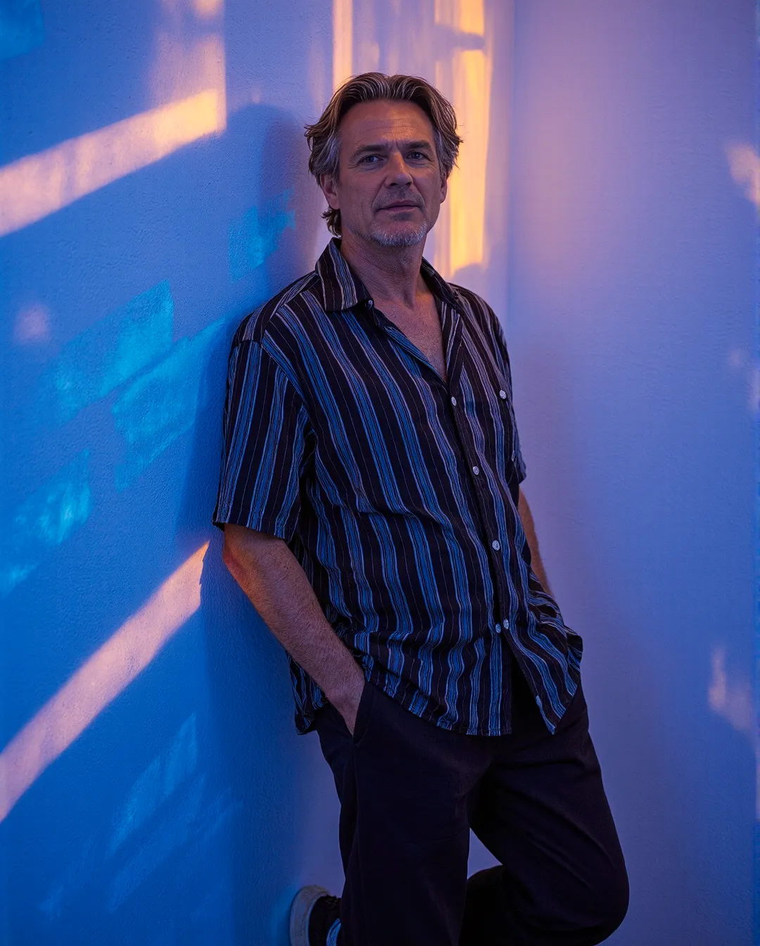Portrait with striking blue and amber lighting effects, featuring a person in a striped button-down shirt against a wall with colorful light projections