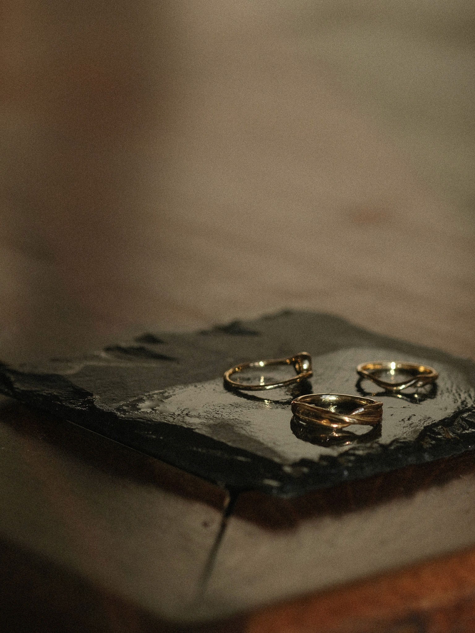 Three gold rings resting on a slab of slate on a dark wood table
