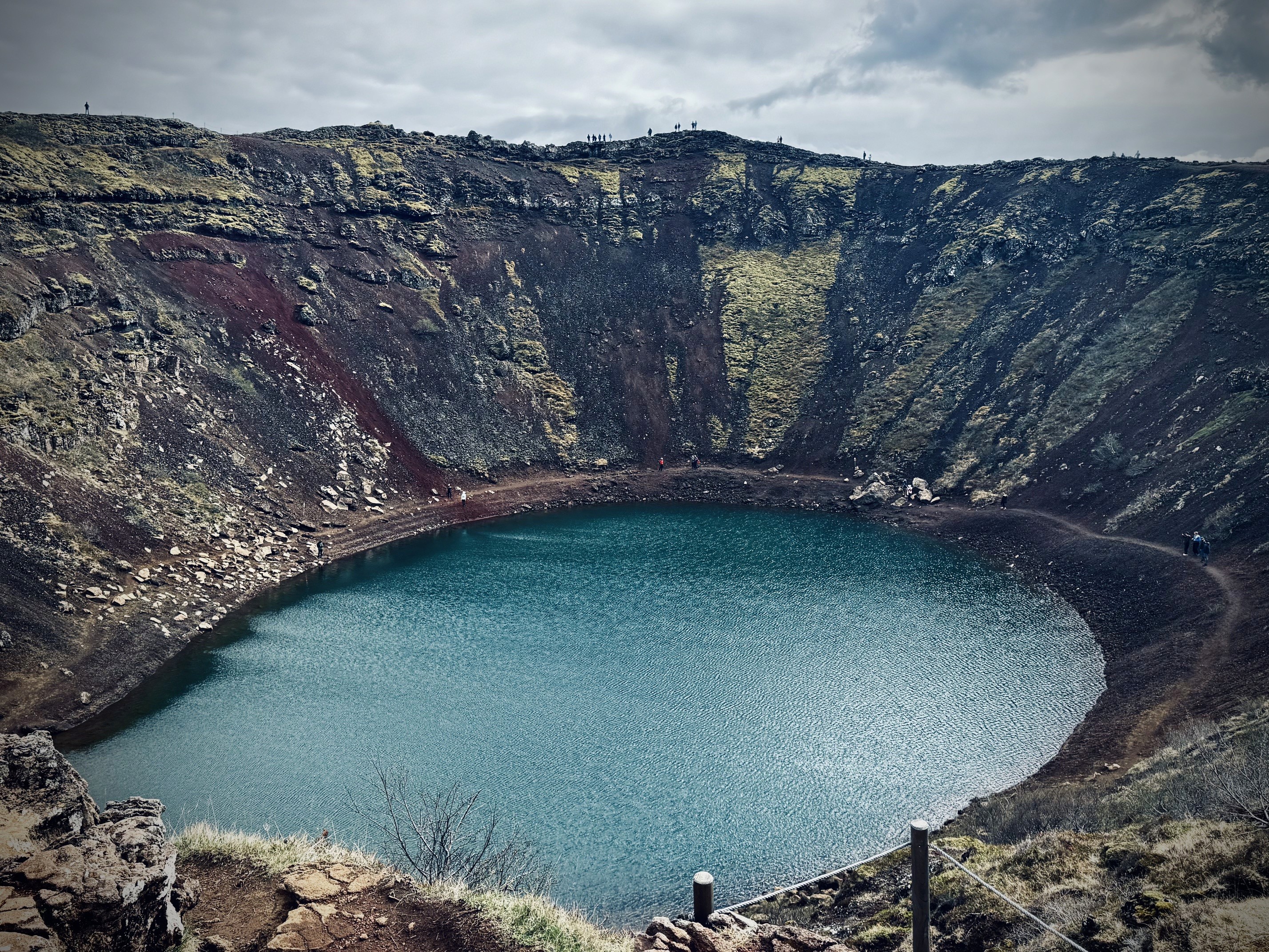 Looking down into Kerid Crater in Iceland, with a blue lake in the middle surrounded by red slopes on all sides.