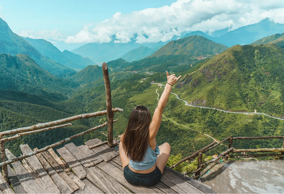 Woman seated on a wooden platform overlooking a mountain valley