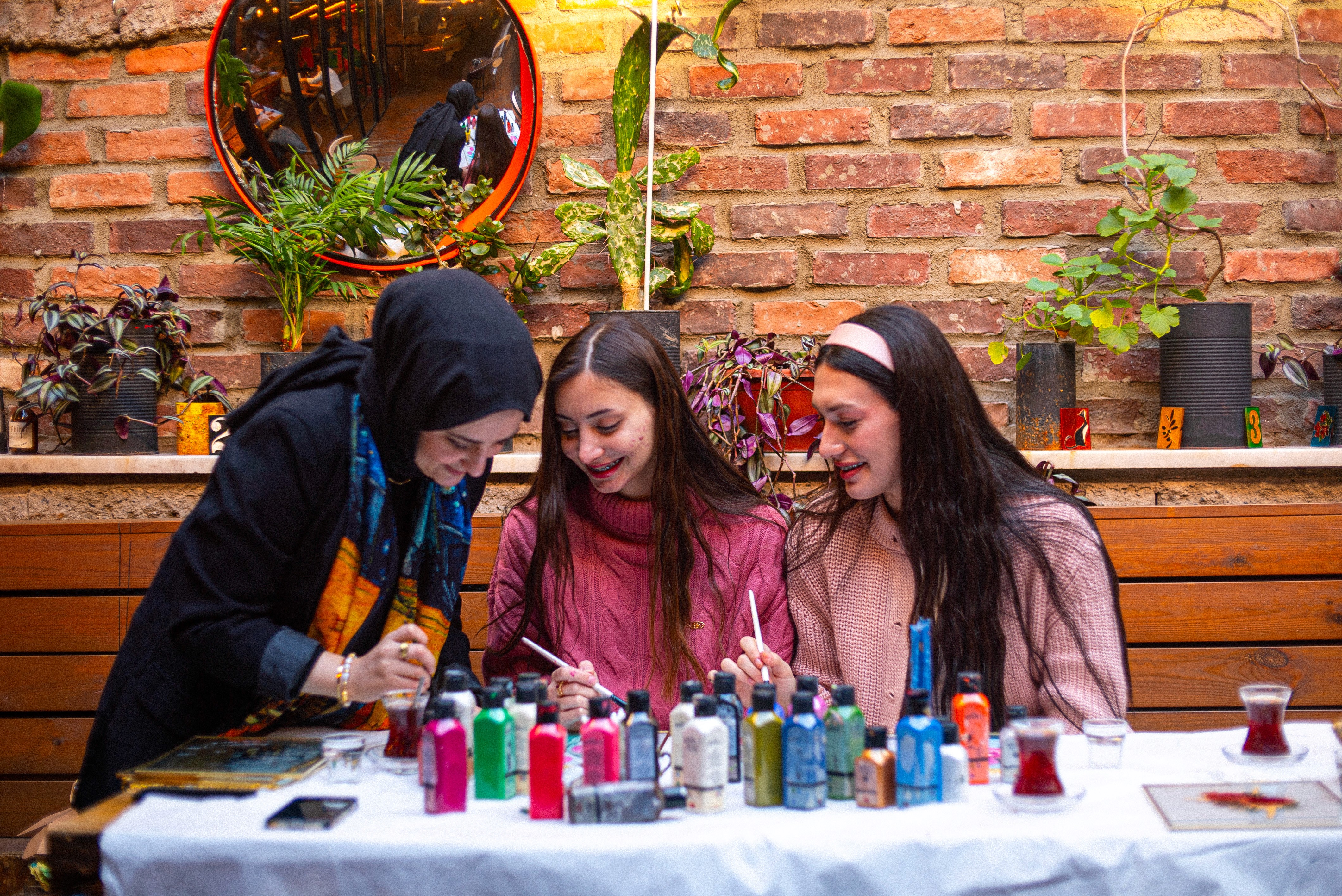 A man and a woman deeply engaged in their stained glass painting projects, with various bottles of paint and tools on the table, representing the immersive experience of this workshop in Istanbul.