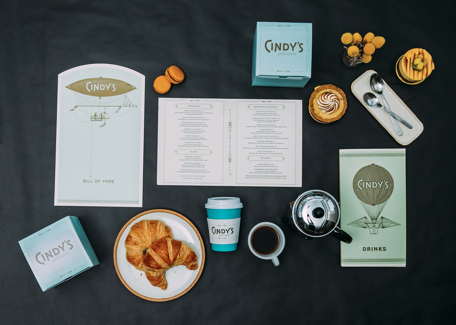 Cindy's menus, pastry box, and coffee sleeve, styled with French press coffee, spoons, and Pastries