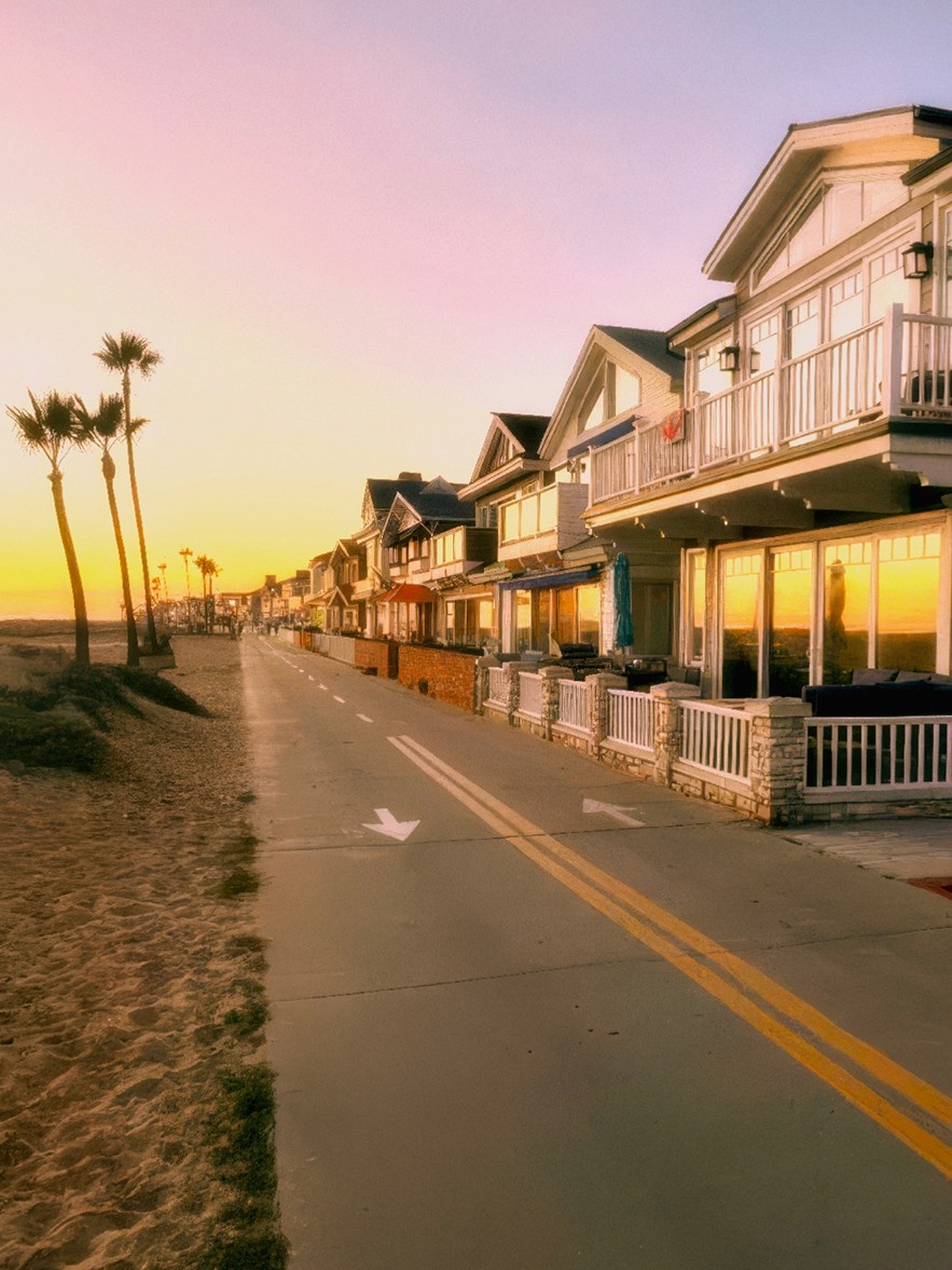 A row of pastel beach houses and palm trees along a coastal walkway at magic hour, glowing under a soft pink-to-amber gradient sky — the roadside Americana light that inspired Retrica's MAGIC preset series