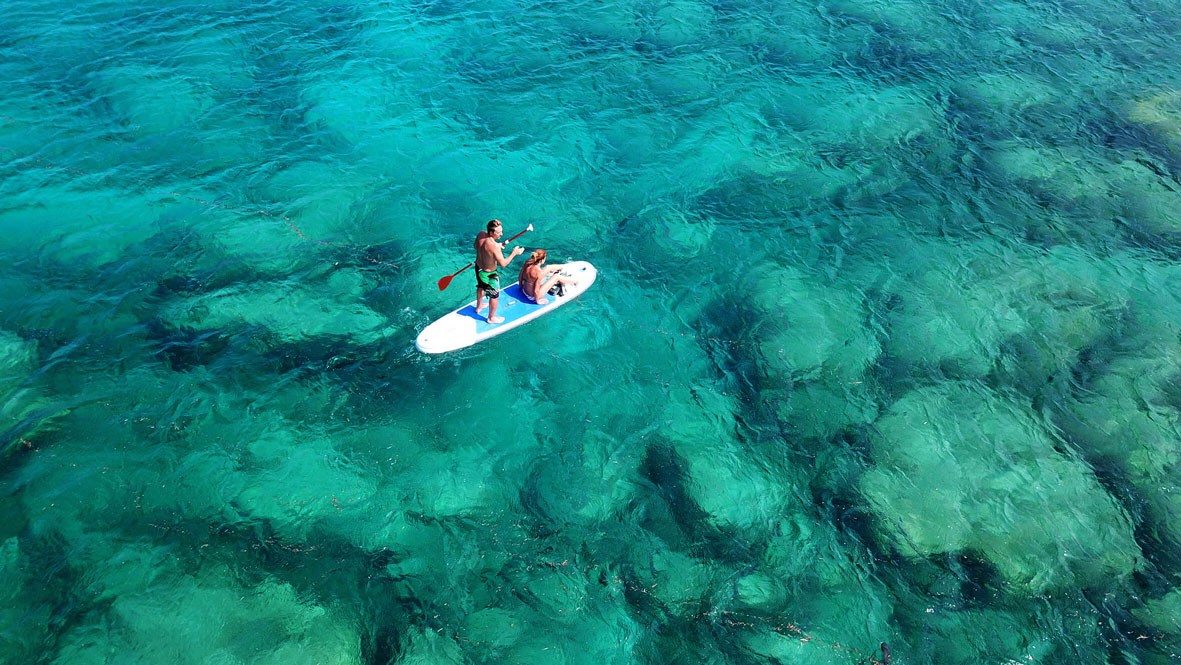 A man is paddleboarding in the shallow coastal waters