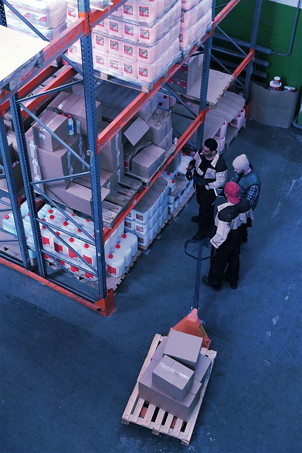 A distant shot of a group of people working in a warehouse, surrounded by tall shelves filled with boxes and equipment.