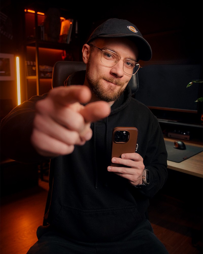 Fotografia portretowa przedstawiająca Krzysztofa Creo w jego biurze, trzymającego telefon i wskazującego palcem odbiorcę (Ciebie)