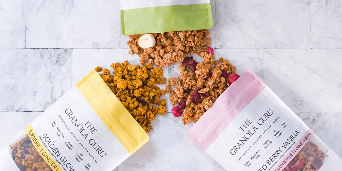 Three varieties of The Granola Guru’s granola: Golden Glow, Mixed Berry Vanilla, and Turmeric Ginger, scattered on marble.