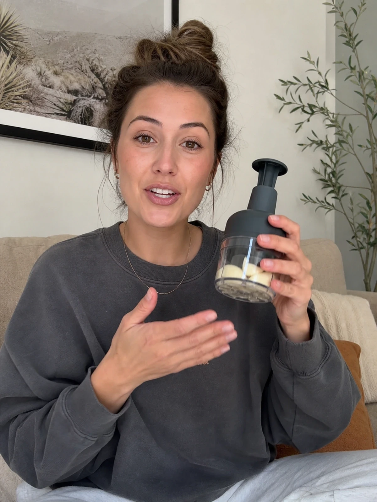 UGC-style photo: home cook creator, on a sofa at home, demonstrating a simple hand-sized product while talking to camera, phone-on-tripod angle.