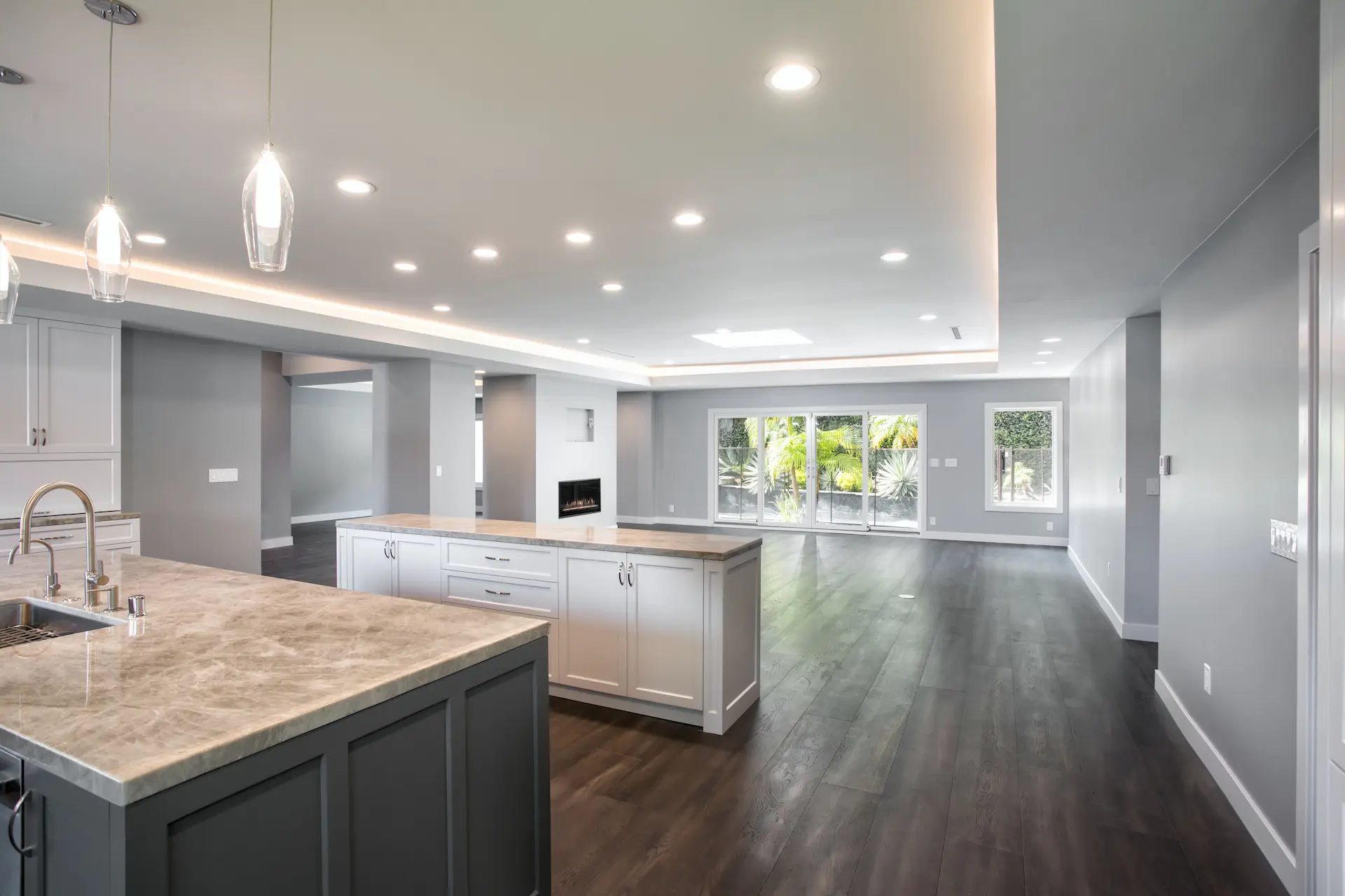 Modern kitchen with gray cabinets, white countertops, and wooden floors; view towards living area in Costa Mesa Remodel. Photo by Chris Darnall.