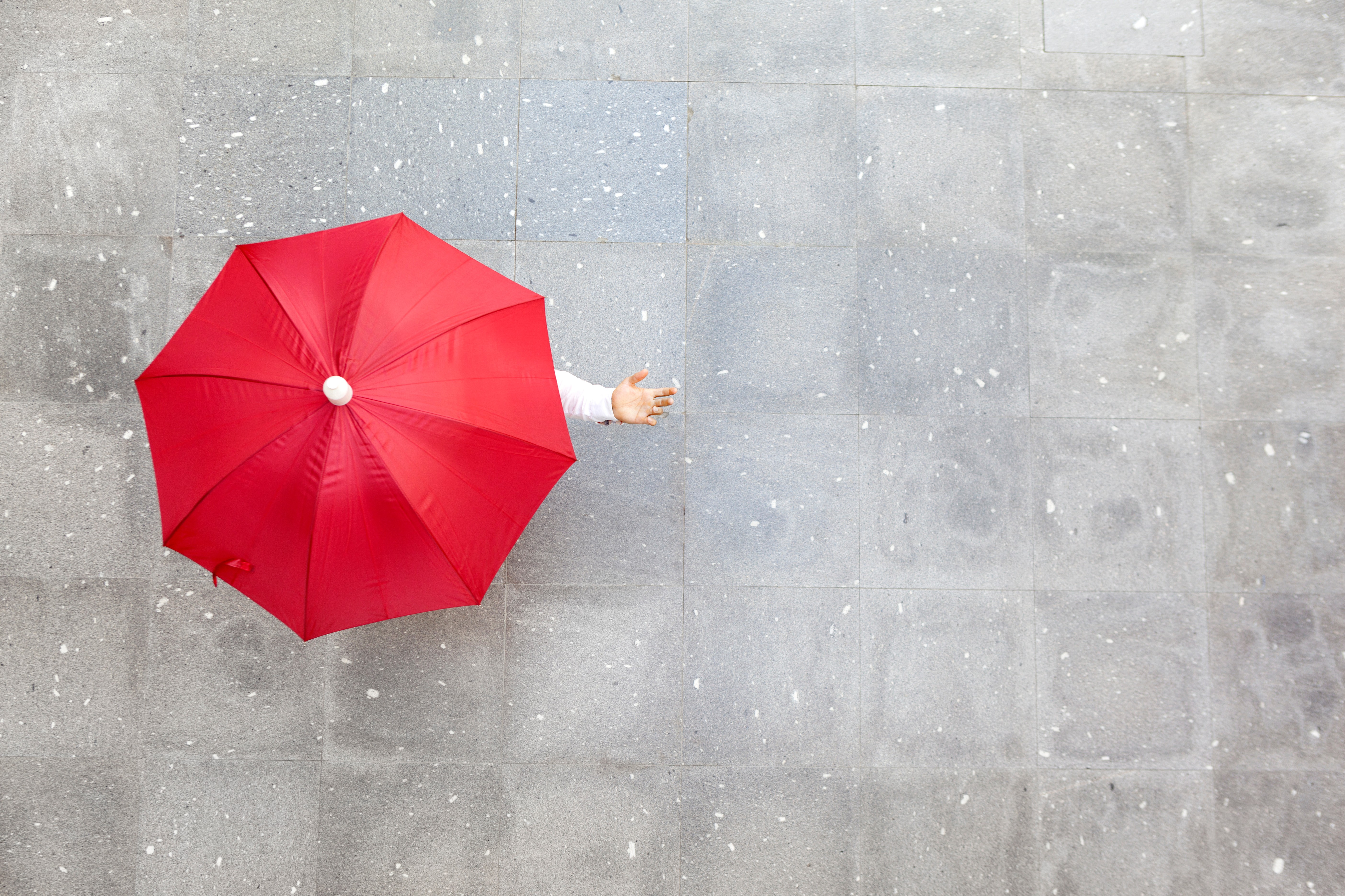 A person holding a red umbrella uses their hand to checks to see if it is snow