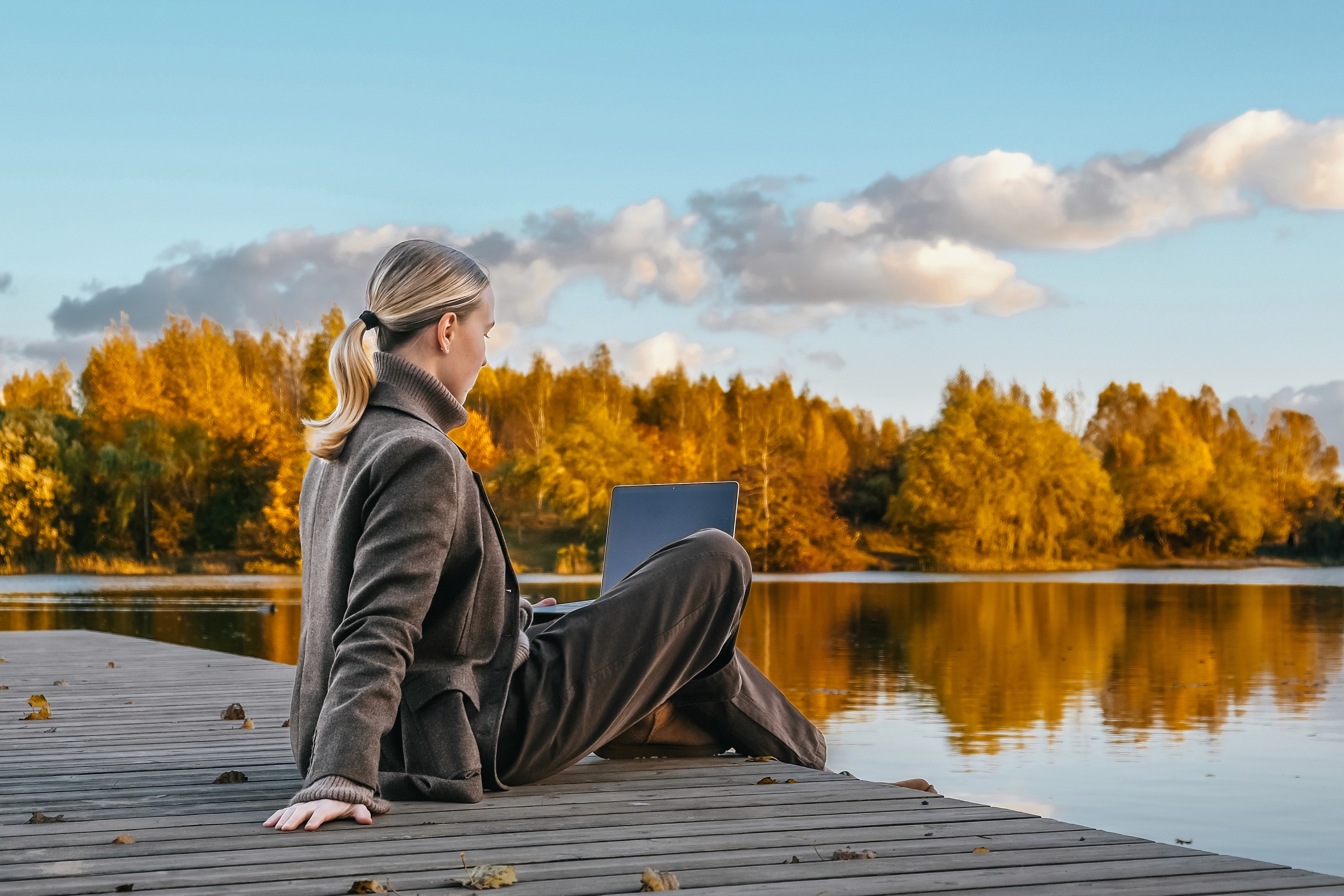 Older man in glasses sitting with laptop on coffee table, smiling while working.