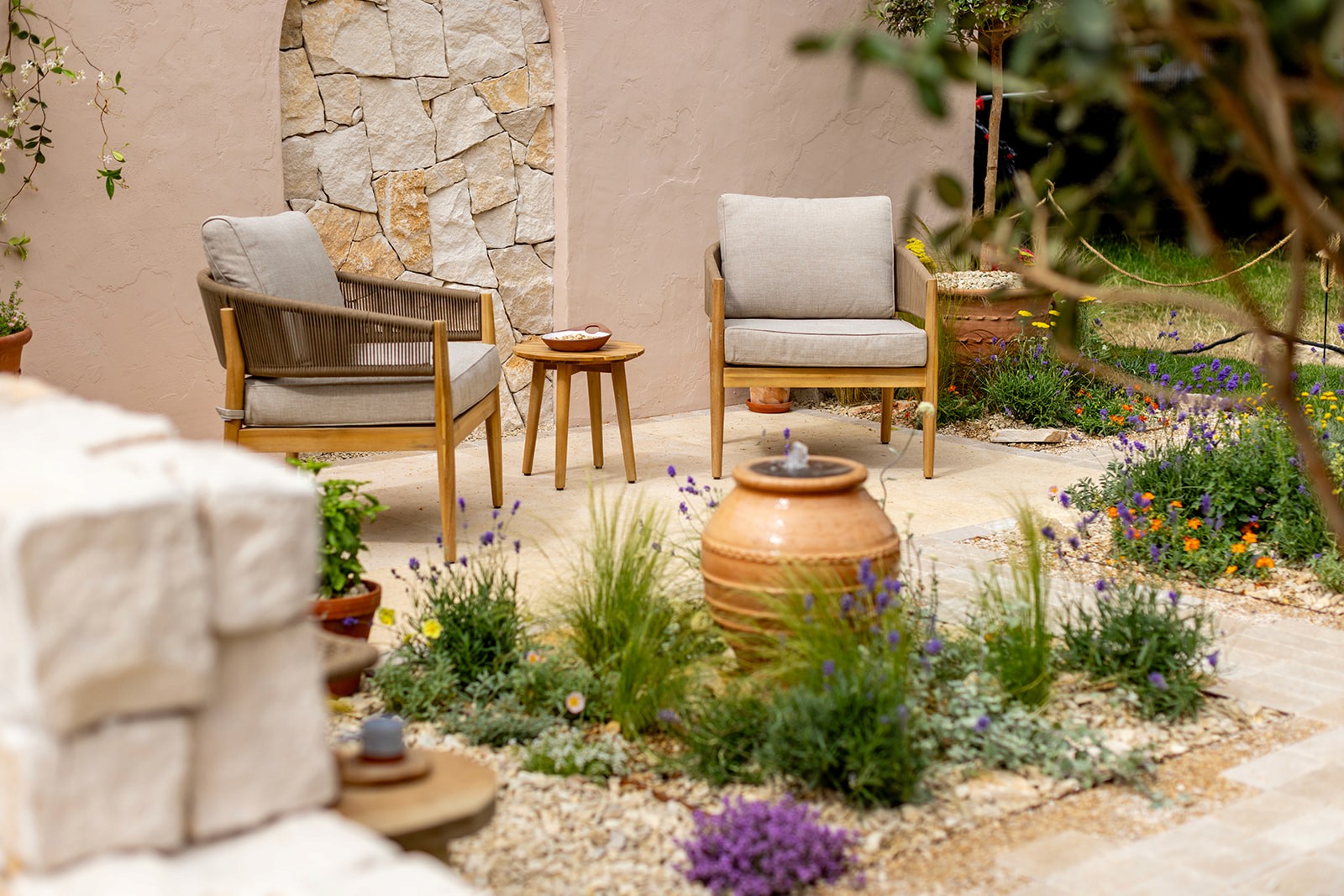 A serene outdoor space featuring two wooden chairs, plants, and a stone wall, creating a cozy atmosphere.
