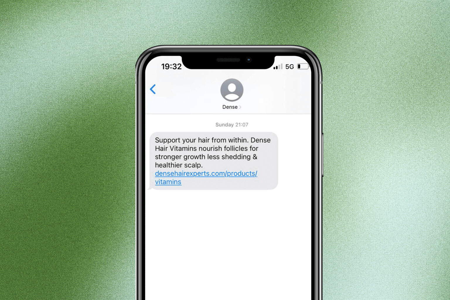 Young man in a green hoodie holding a yellow phone while seated at a table with a tablet.