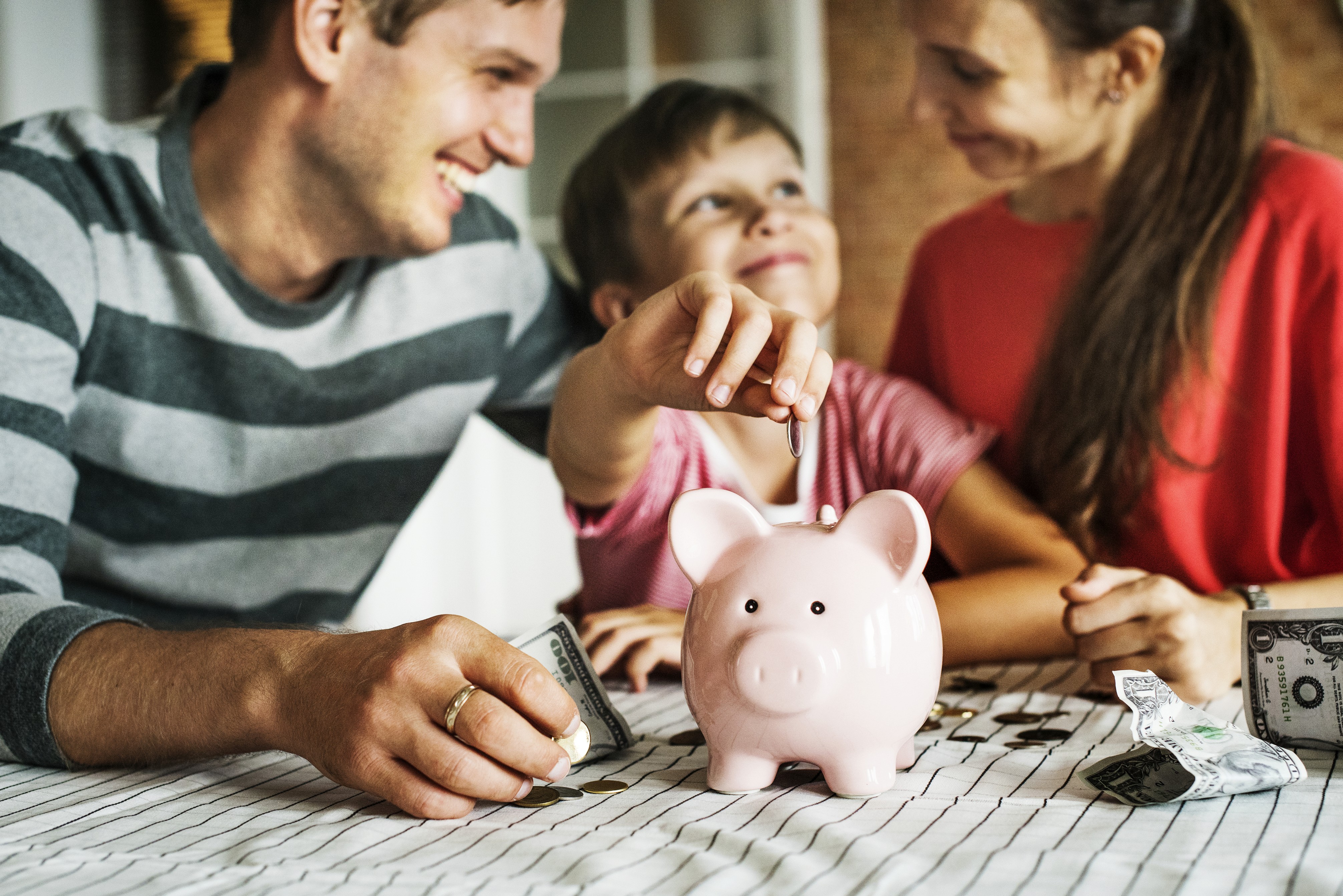 Familie legt gemeinsam Geld in ein rosa Sparschwein – Eltern und Kind sparen spielerisch für die Zukunft und lernen den Umgang mit Geld.