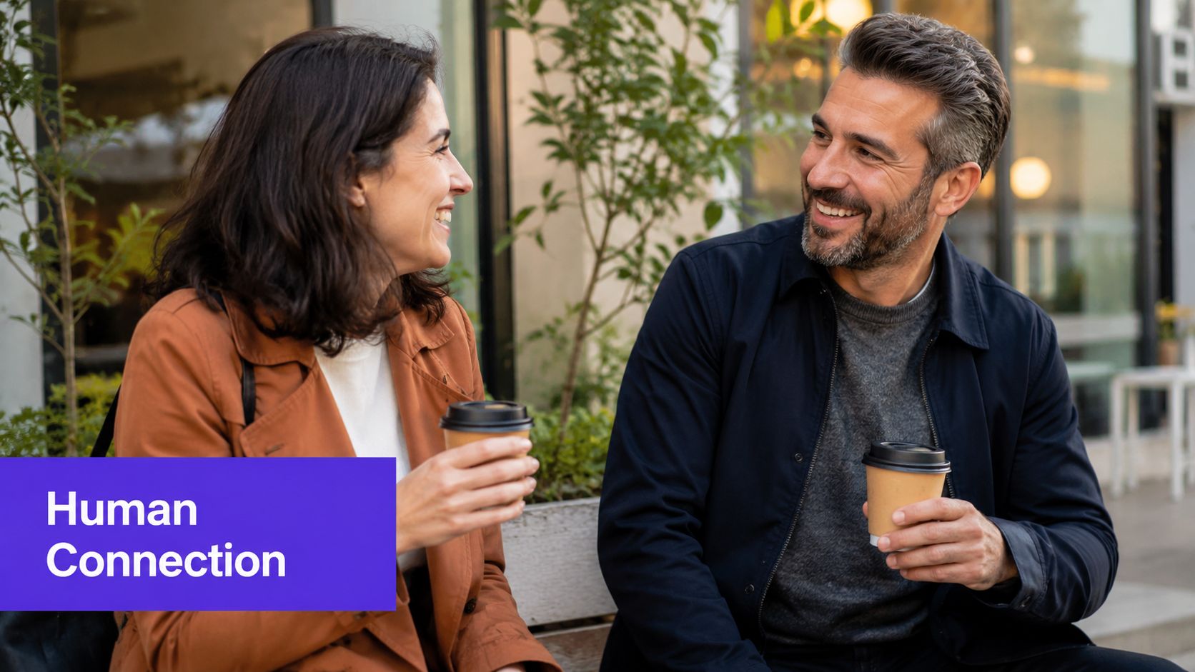 A woman and a man laughing while having a friendly conversation and holding coffee cups outdoors.