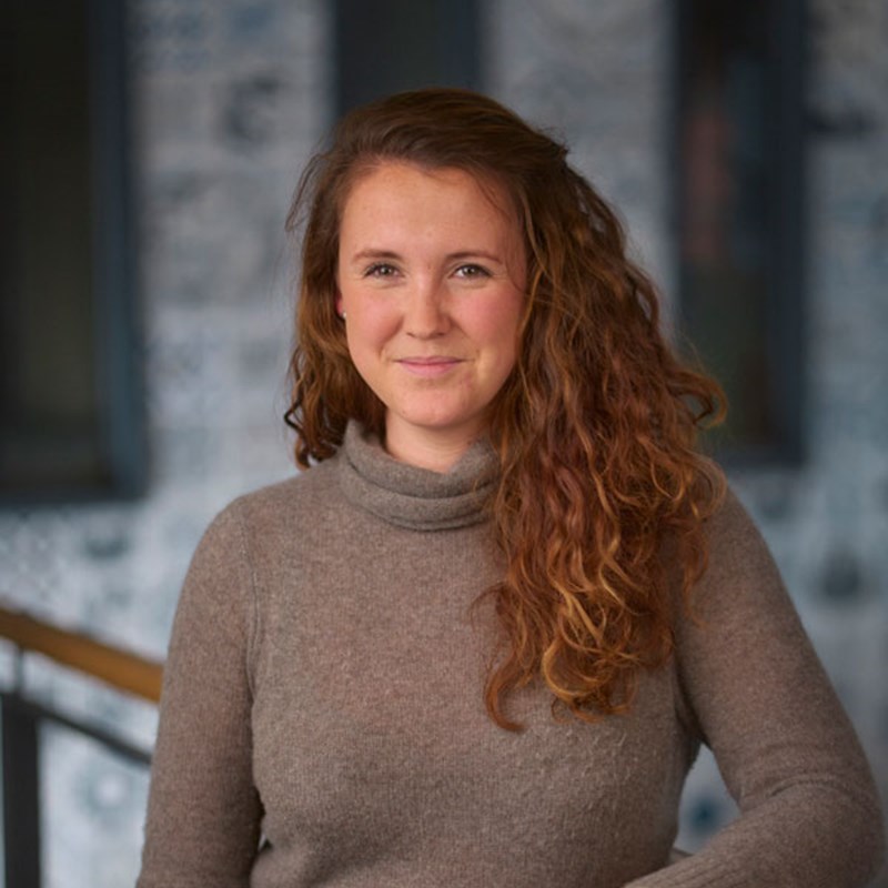 Colour photograph of woman with brown long curly hair and brown jumper.