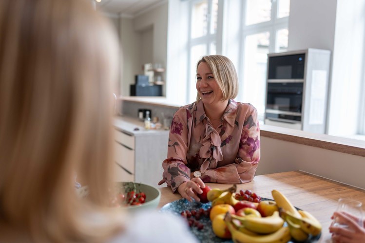 Geschäftsführerin in gemusterter Bluse sitzt an einem Tisch und spricht mit einer gegenüber sitzenden Person im Büro von SLB.