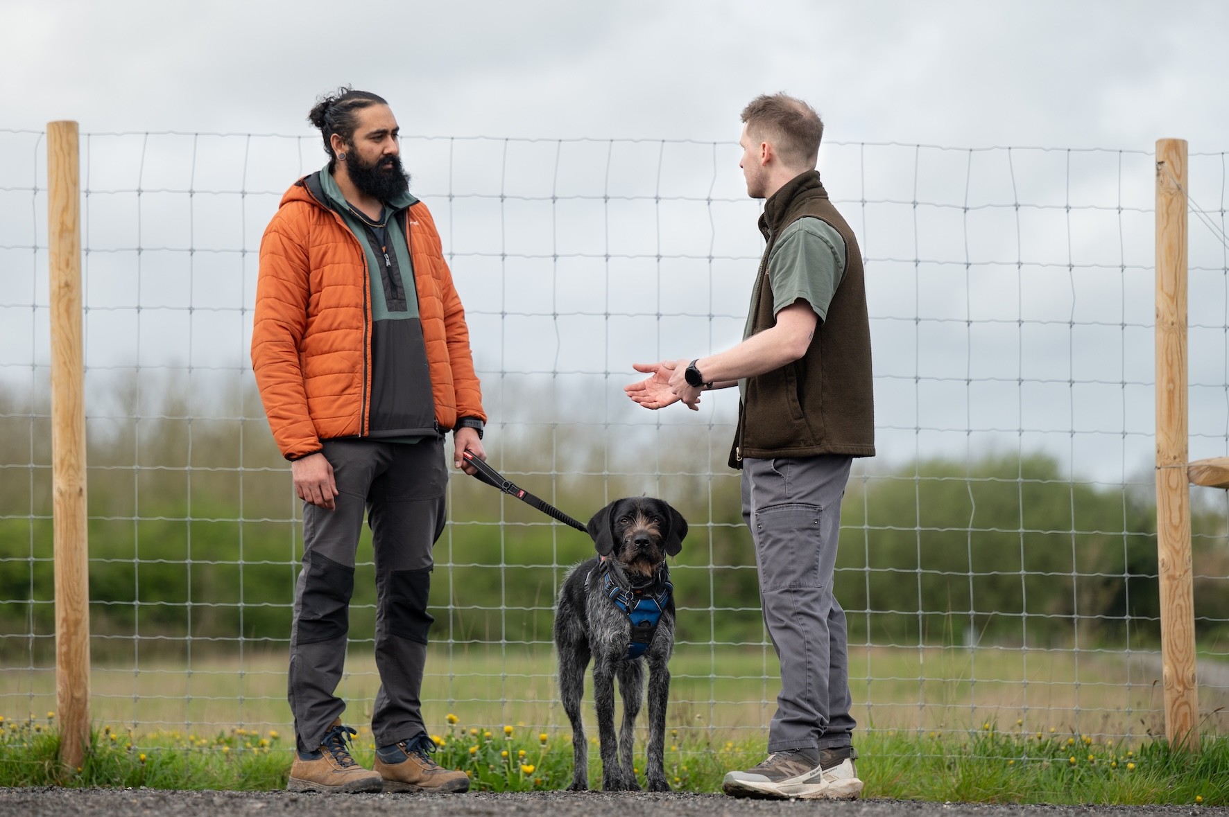A happy, relaxed dog is stood between their owner & Scott (Dog Person). The owner & Scott are talking, while the dog is focussed on the camera