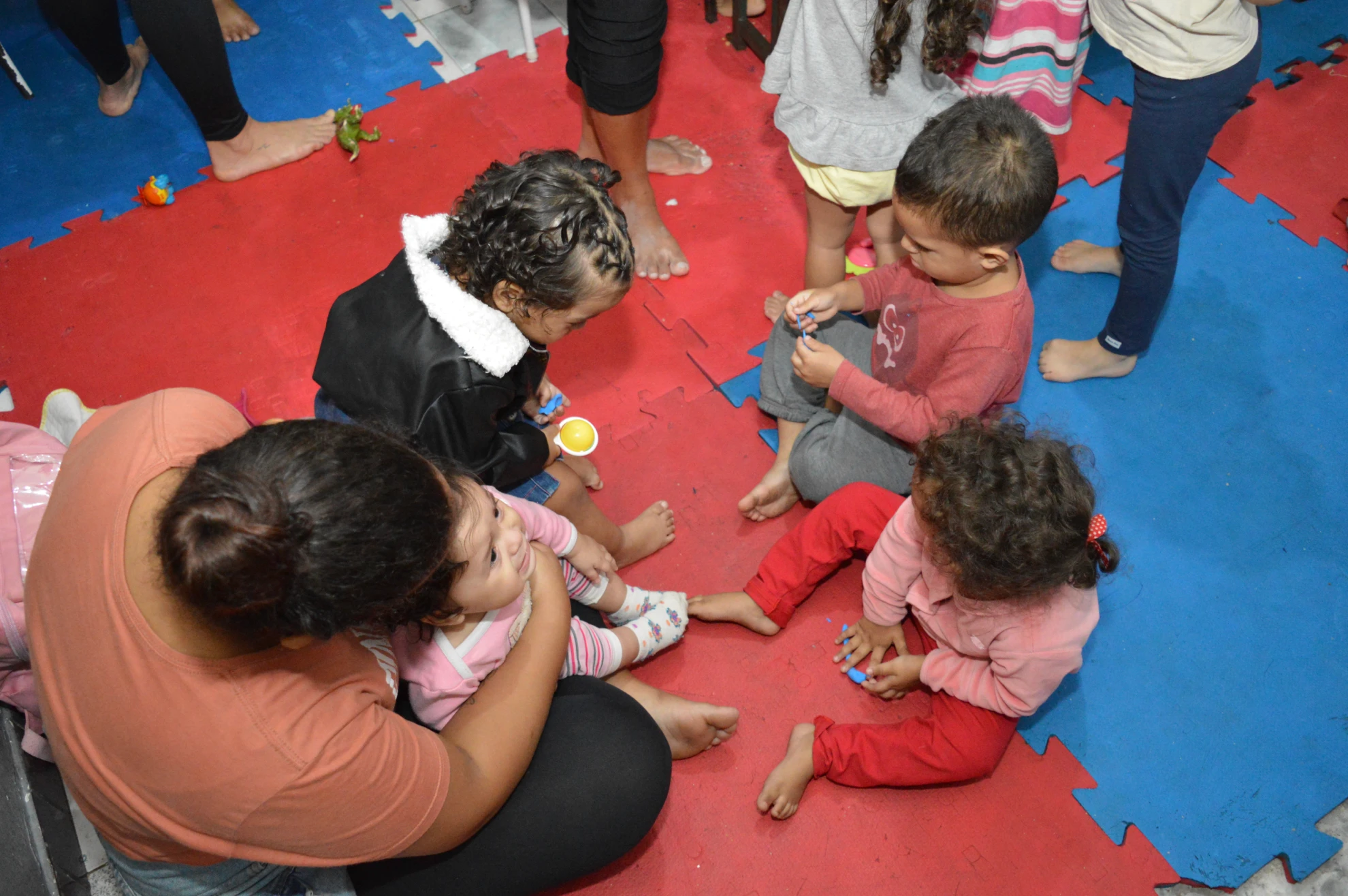 Crianças pequenas sentadas no tapete interagindo com uma voluntária.