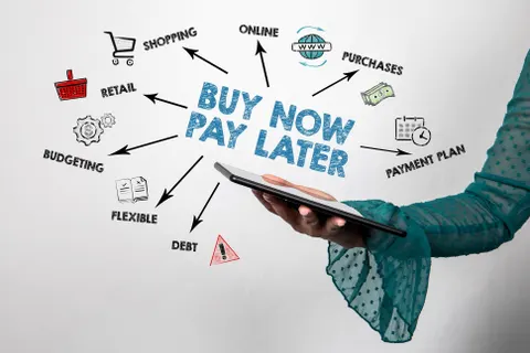 Hand mit Tablet und dem Schriftzug „Buy Now Pay Later“, Pfeile zeigen auf Begriffe wie Einkaufen, Schulden und Handel. Weißer Hintergrund.