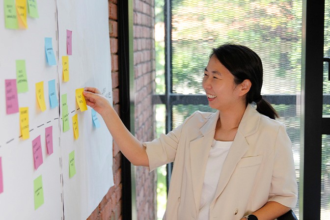 A side profile image of our team member, Hye Yoon, who's sticking a yellow post-it note on the whiteboard.