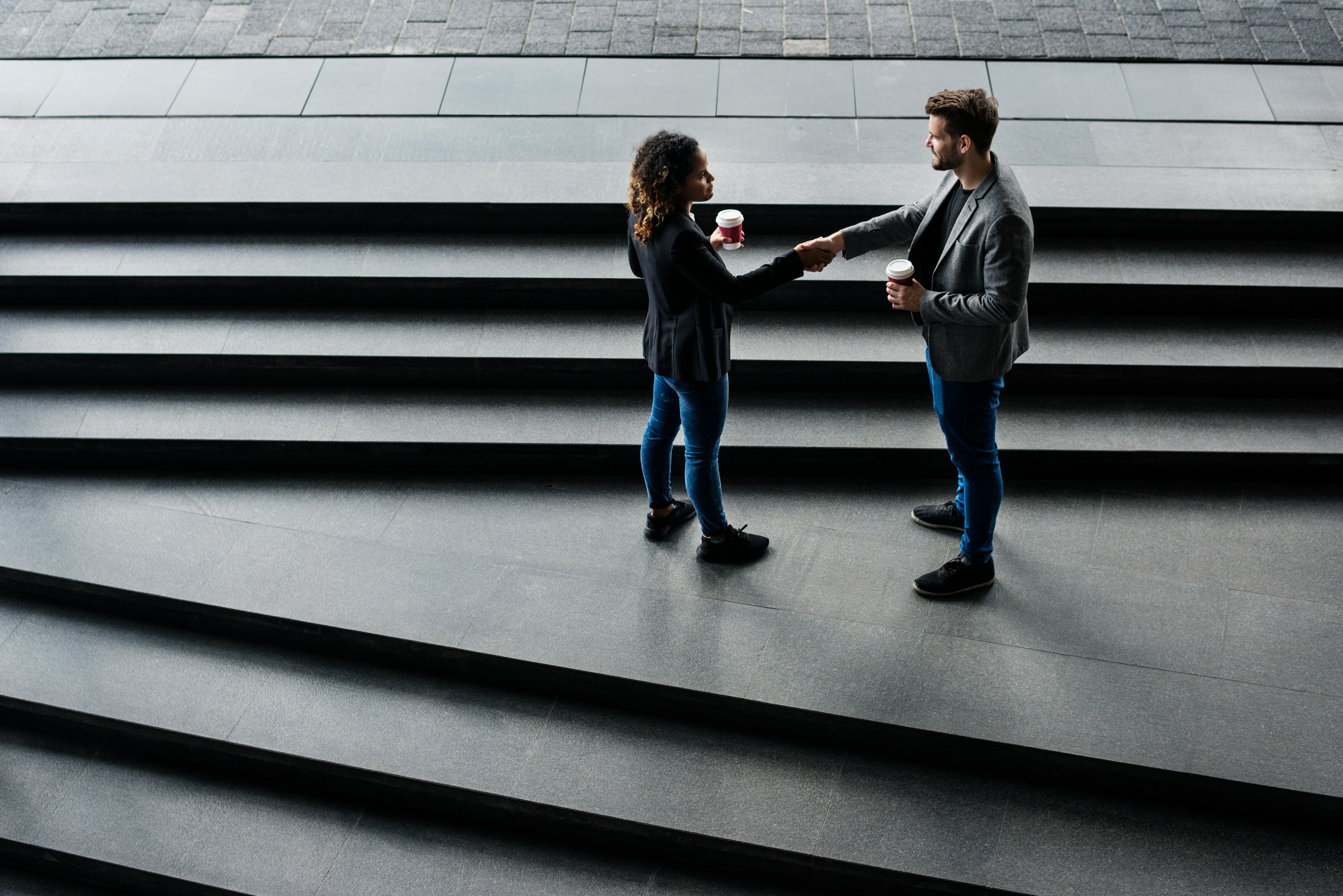 Two business people shaking hands whilst holding coffee cups