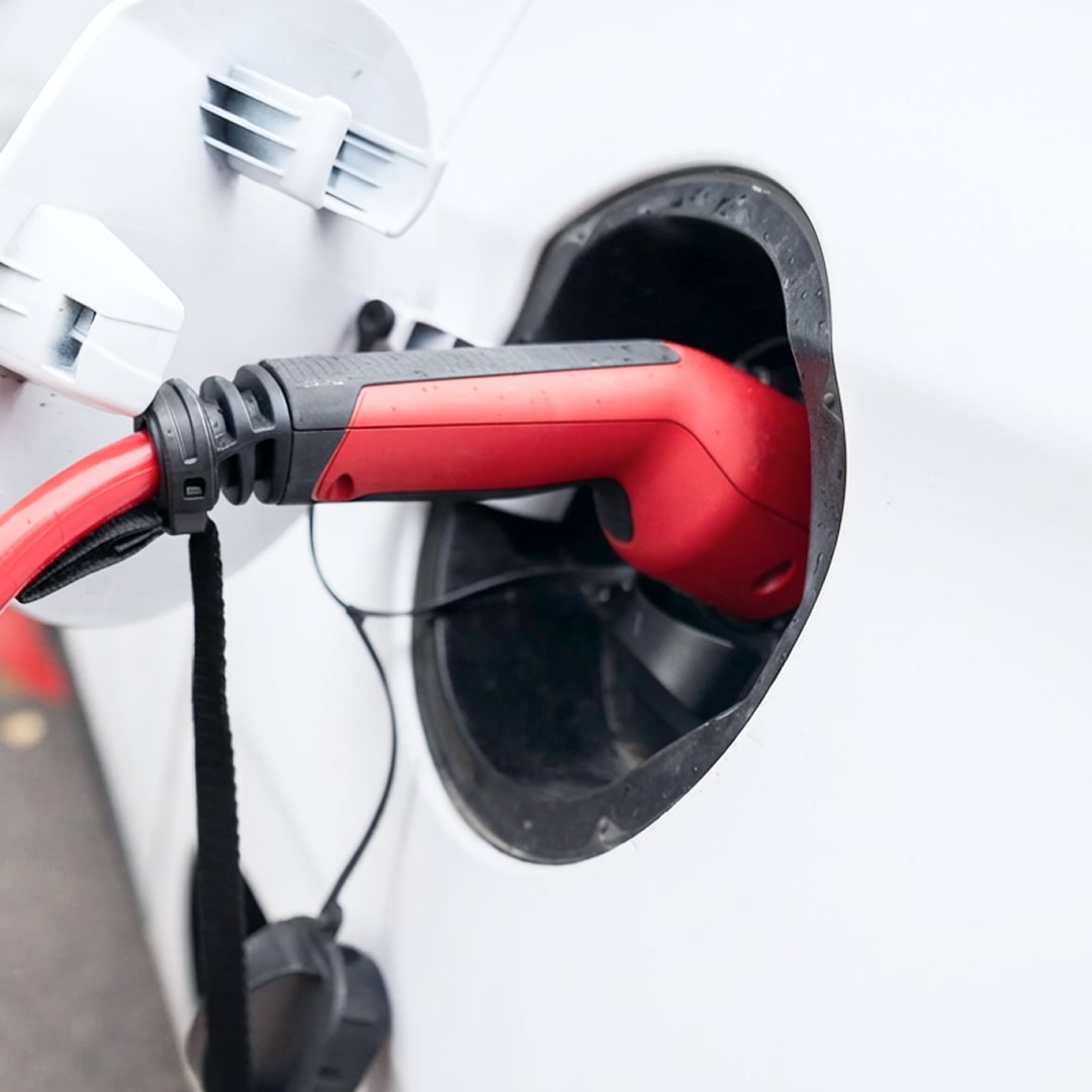 Close-up photograph of a red EV charging connector plugged into the charging port of a white electric vehicle.