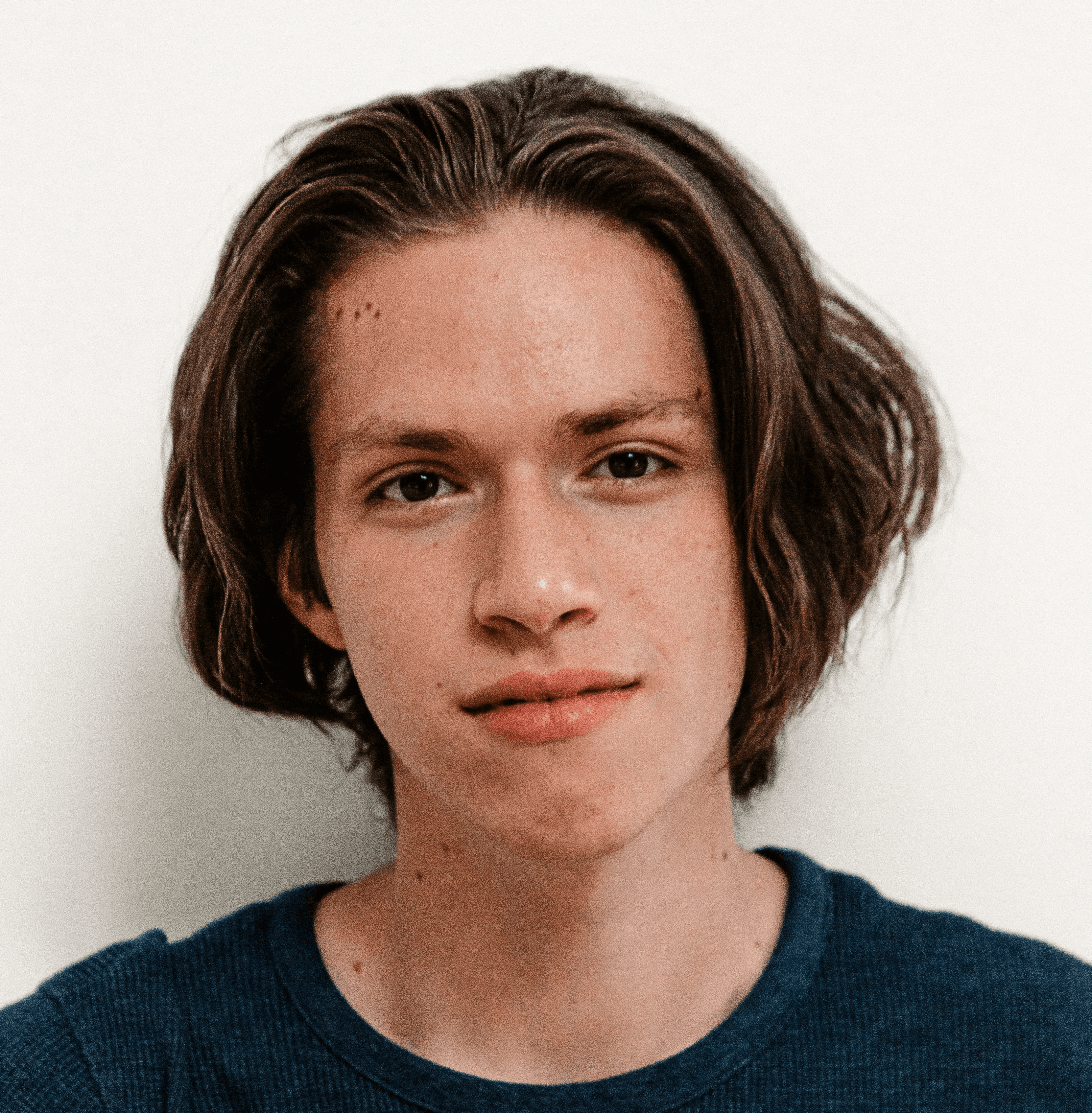A young man with shoulder-length brown hair wearing a dark blue shirt