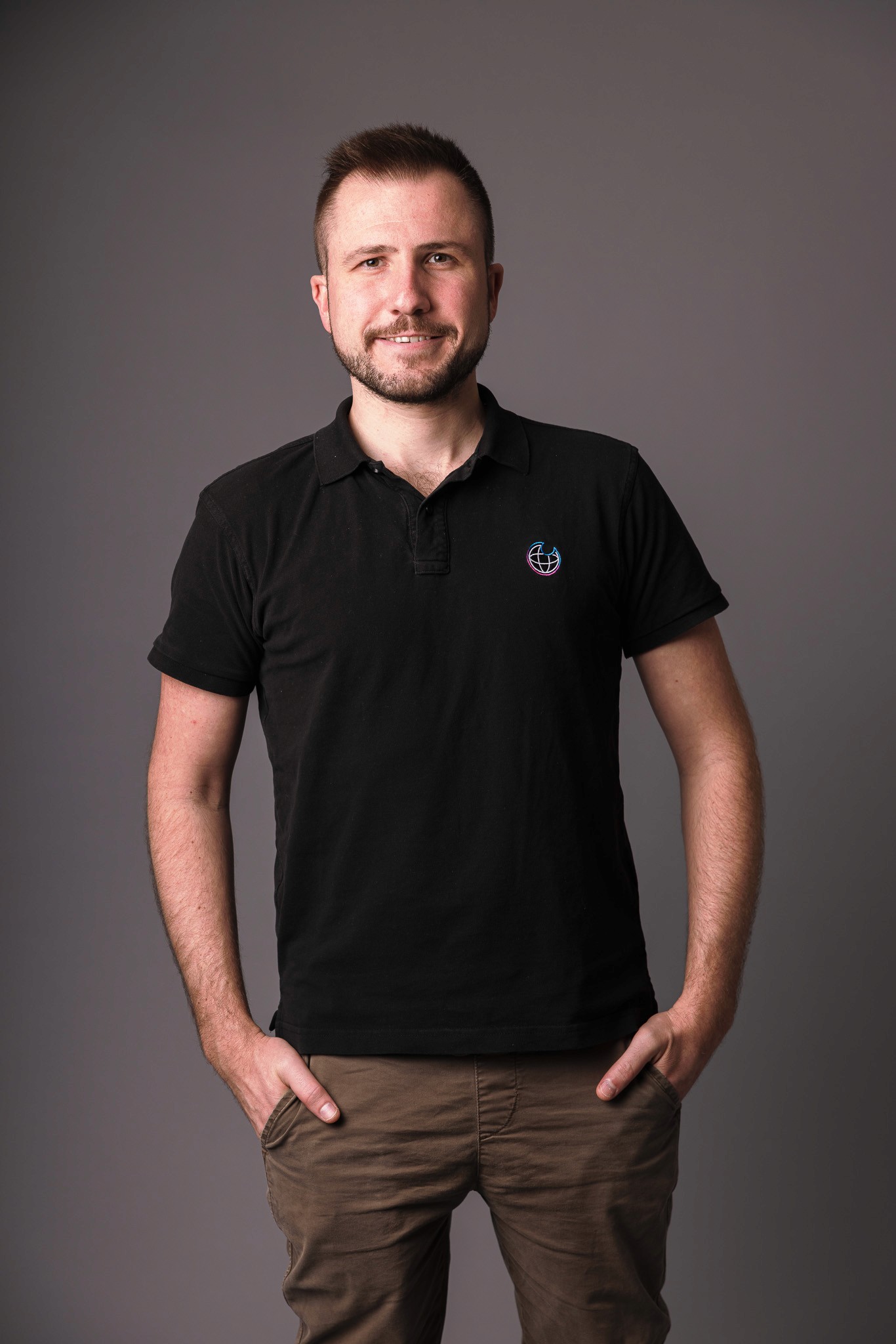 A smiling man with wavy hair and a beard, wearing a green jacket over a black shirt. He stands against a deep red background, conveying a warm, friendly tone.