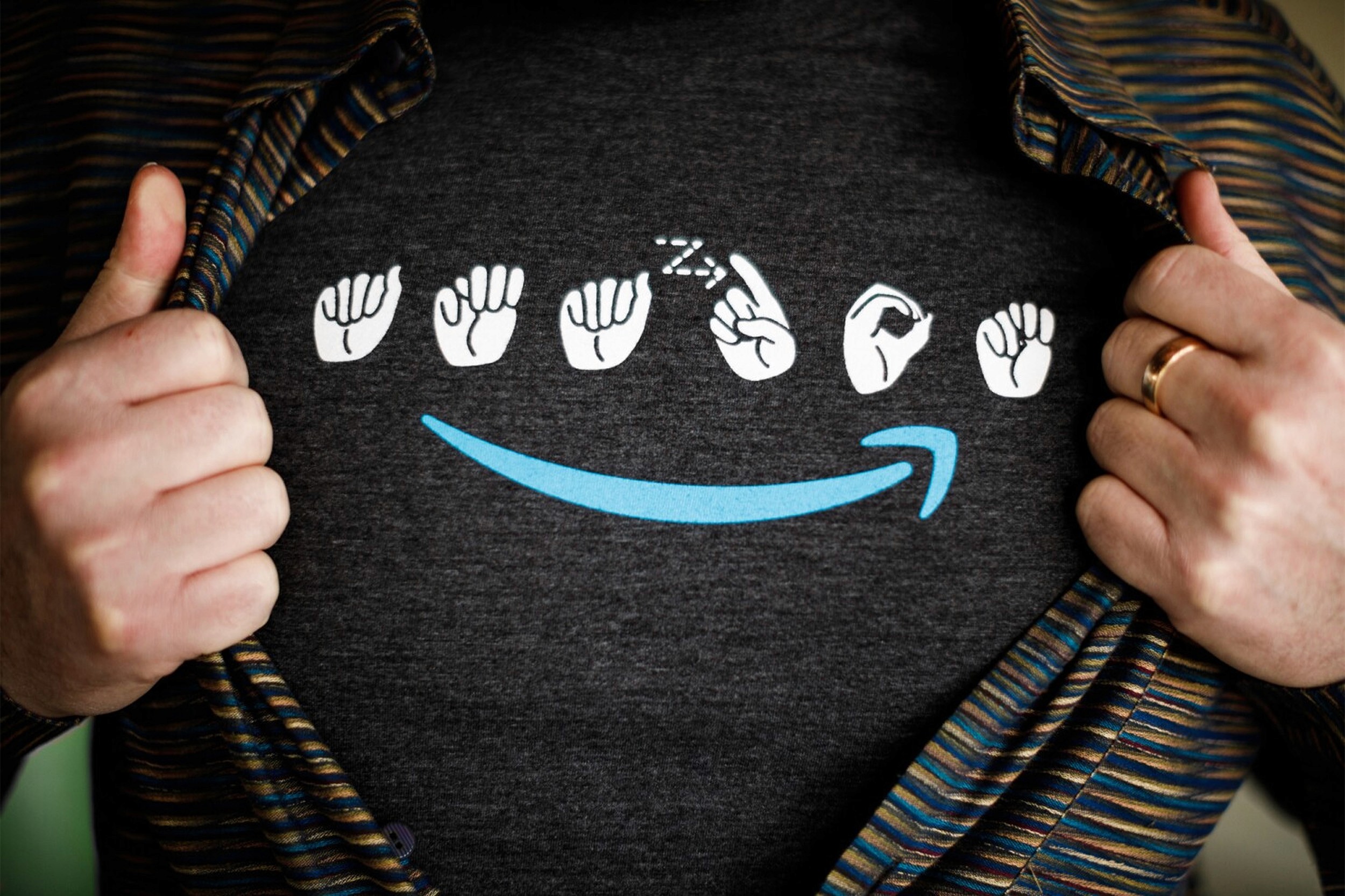 Close-up of a buttoned shirt being opened up to reveal a t-shirt with "Amazon" logo fingerspelled in American Sign Language.