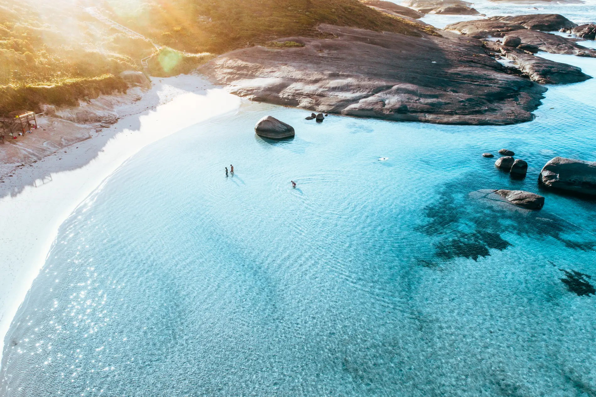 Aerial of a sheltered bay with granite boulders, pale sand and clear turquoise water