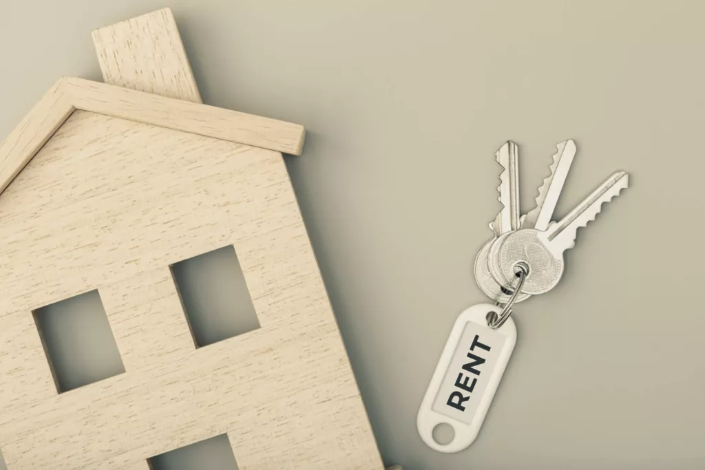Wooden house cut-out and keys with 'RENT' keychain, symbolizing percentage rent agreements.