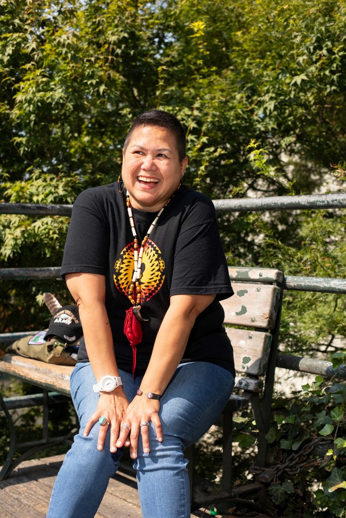 Donna sitting on a park bench in front of foliage.