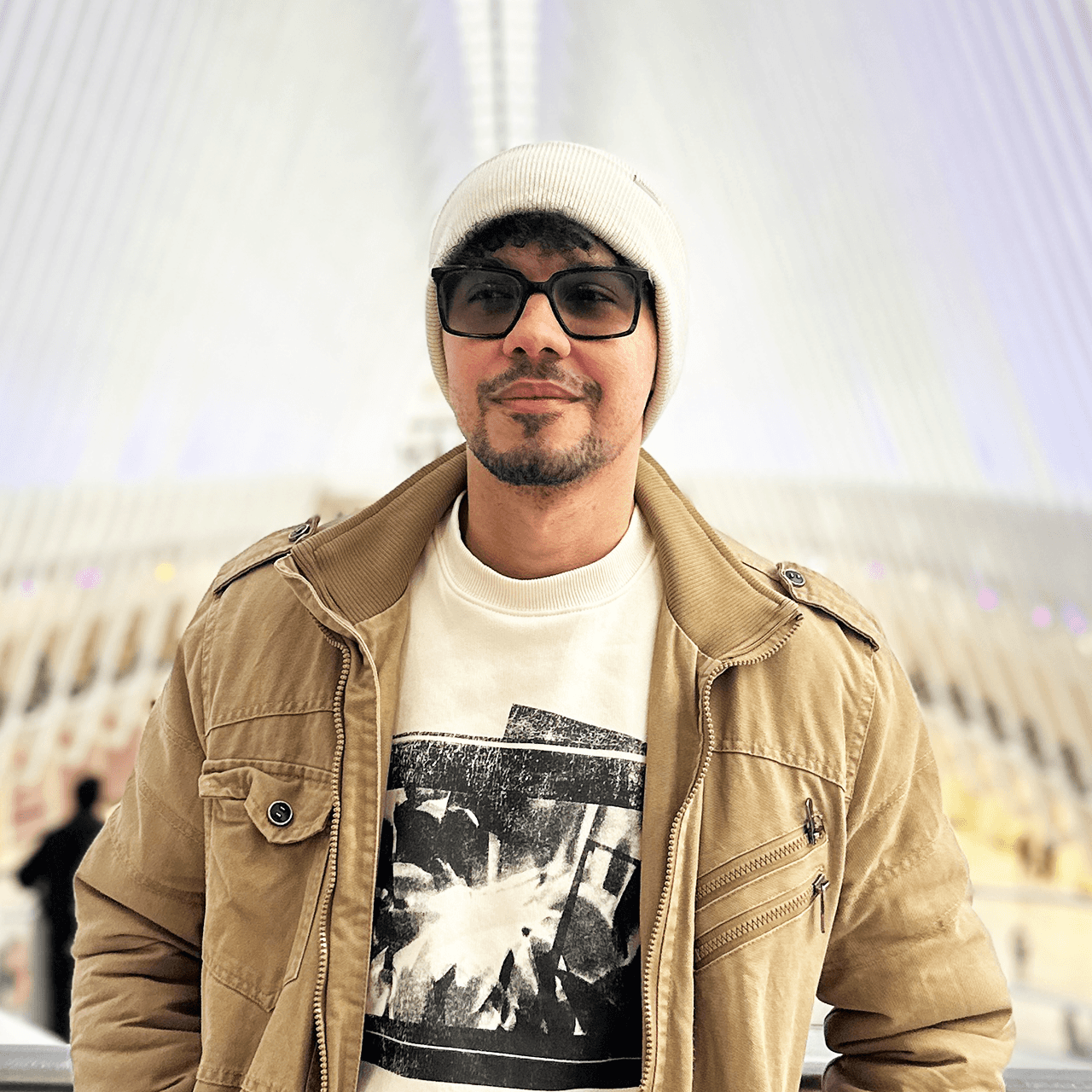 Man with dark hair wearing a black sweater over a collared shirt, softly lit and facing forward
