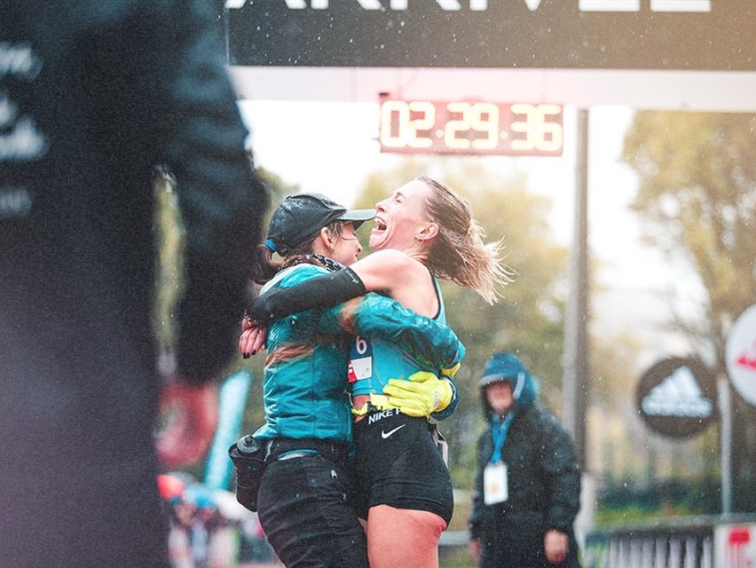 Une coureuse célébrant son arrivée, dans une émotion intense, après avoir franchi la ligne d'arrivée sous la pluie.