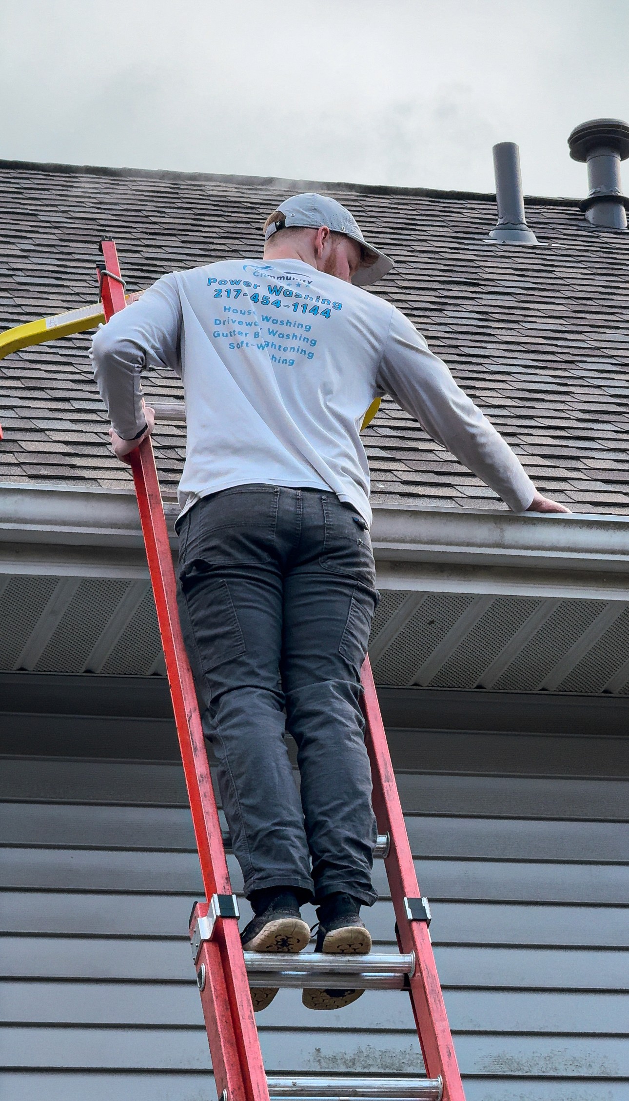 Community Clean technician on a ladder cleaning a home's gutters
