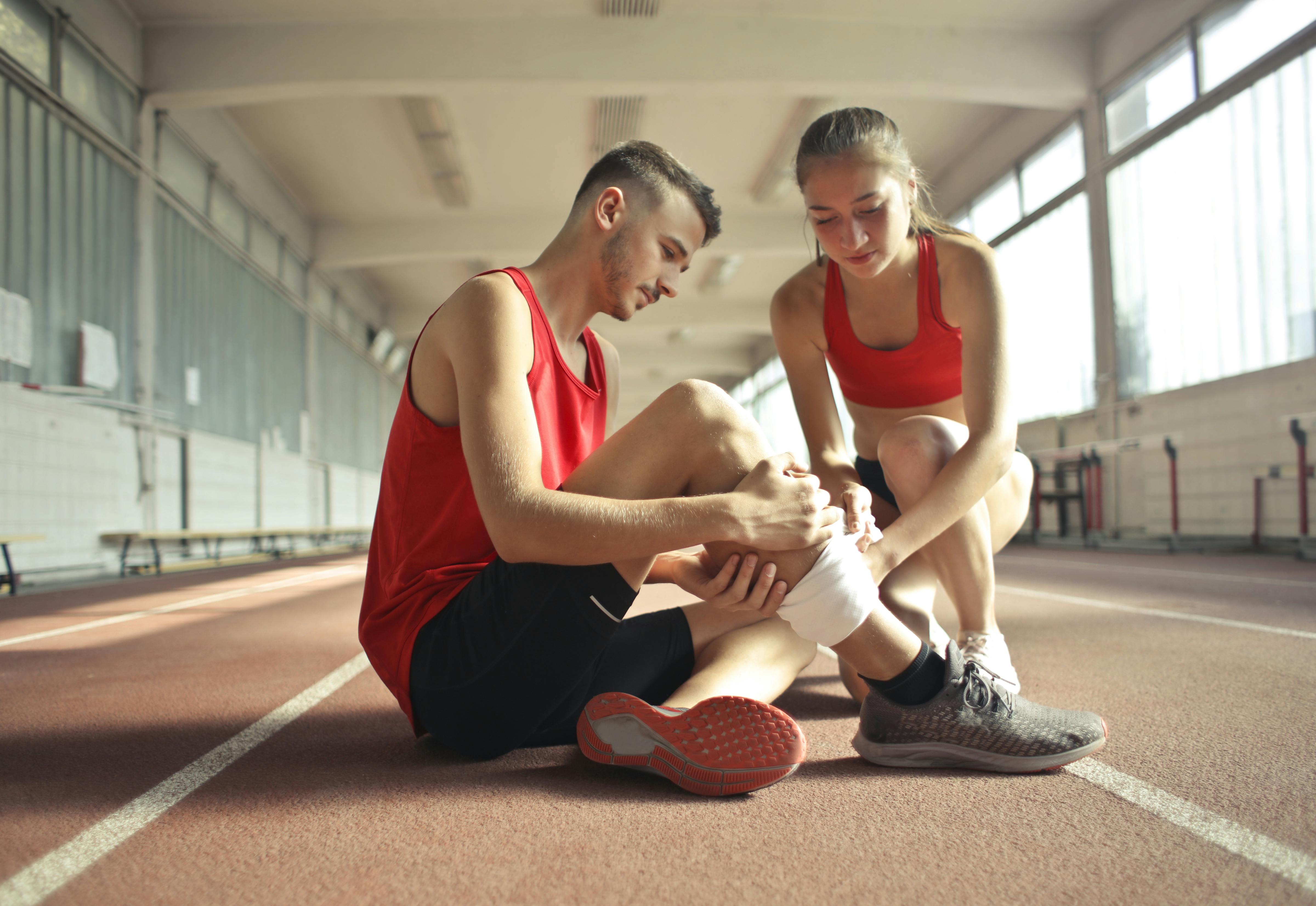 Man injured during a sport event, being helped by another woman athlete