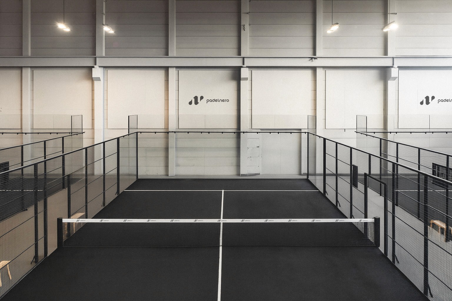 Moderner Indoor-Padelcourt mit schwarzem Boden und Padelnero-Logo an der Wand – minimalistisches Design und klare Linien für ein hochwertiges Spielerlebnis.