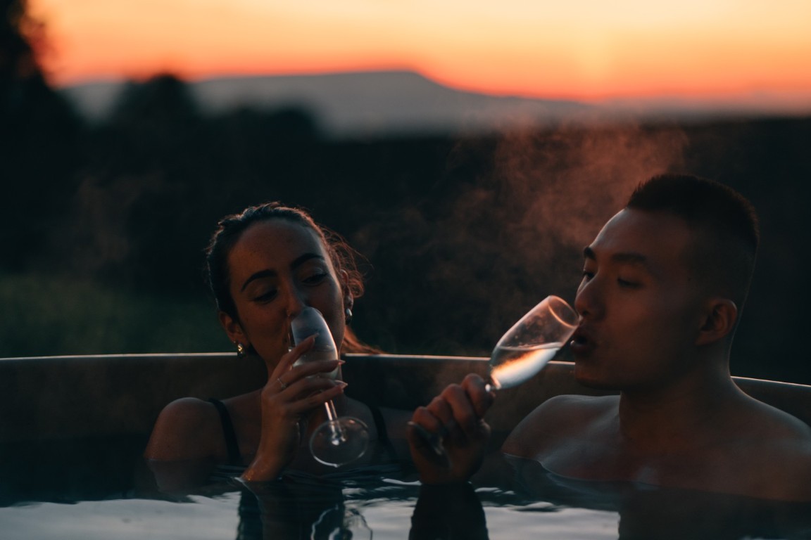 A couple drinking champagne in a hot tub with a sunset in the background.