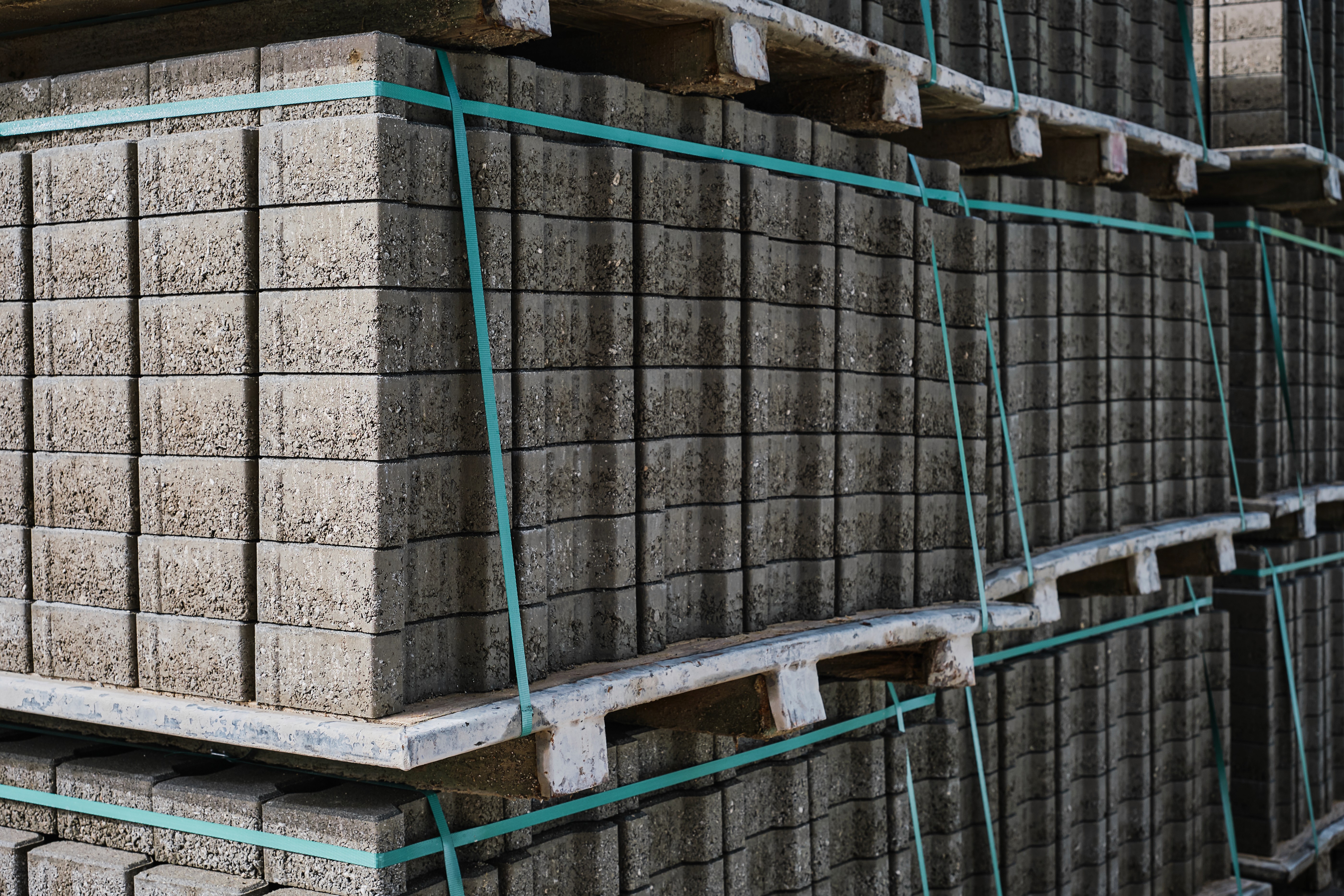 Stacks of gray concrete blocks are tightly bound with blue straps on wooden pallets. The orderly arrangement suggests industrial readiness and strength.