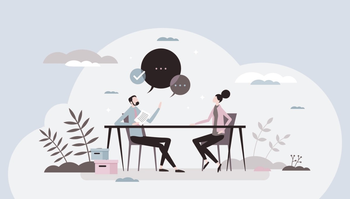 Illustration of two people seated across a table in a professional conversation, one holding a document and speaking while the other listens, with dialogue icons above them and a calm office setting in the background.