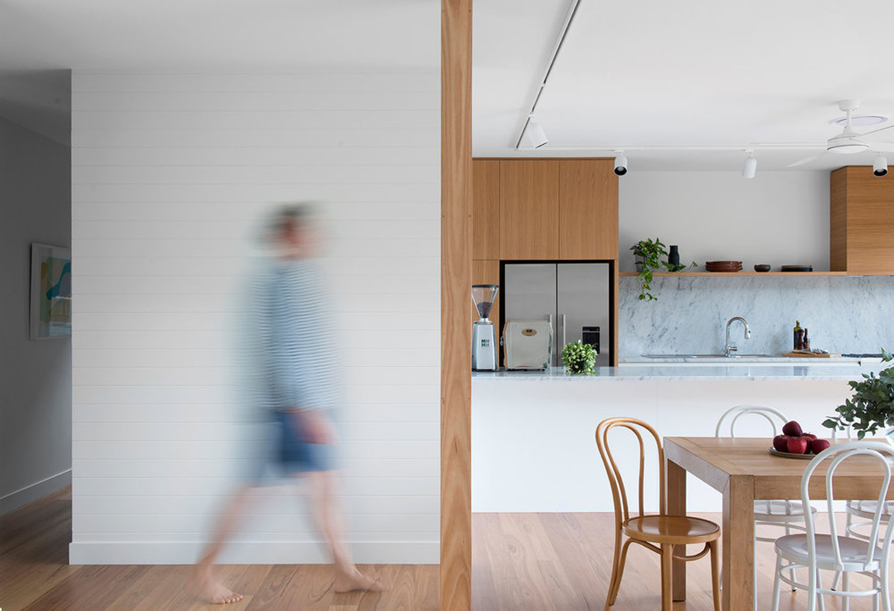 Open-plan living with subtle zoning, timber detailing, and blurred figure capturing movement through space.