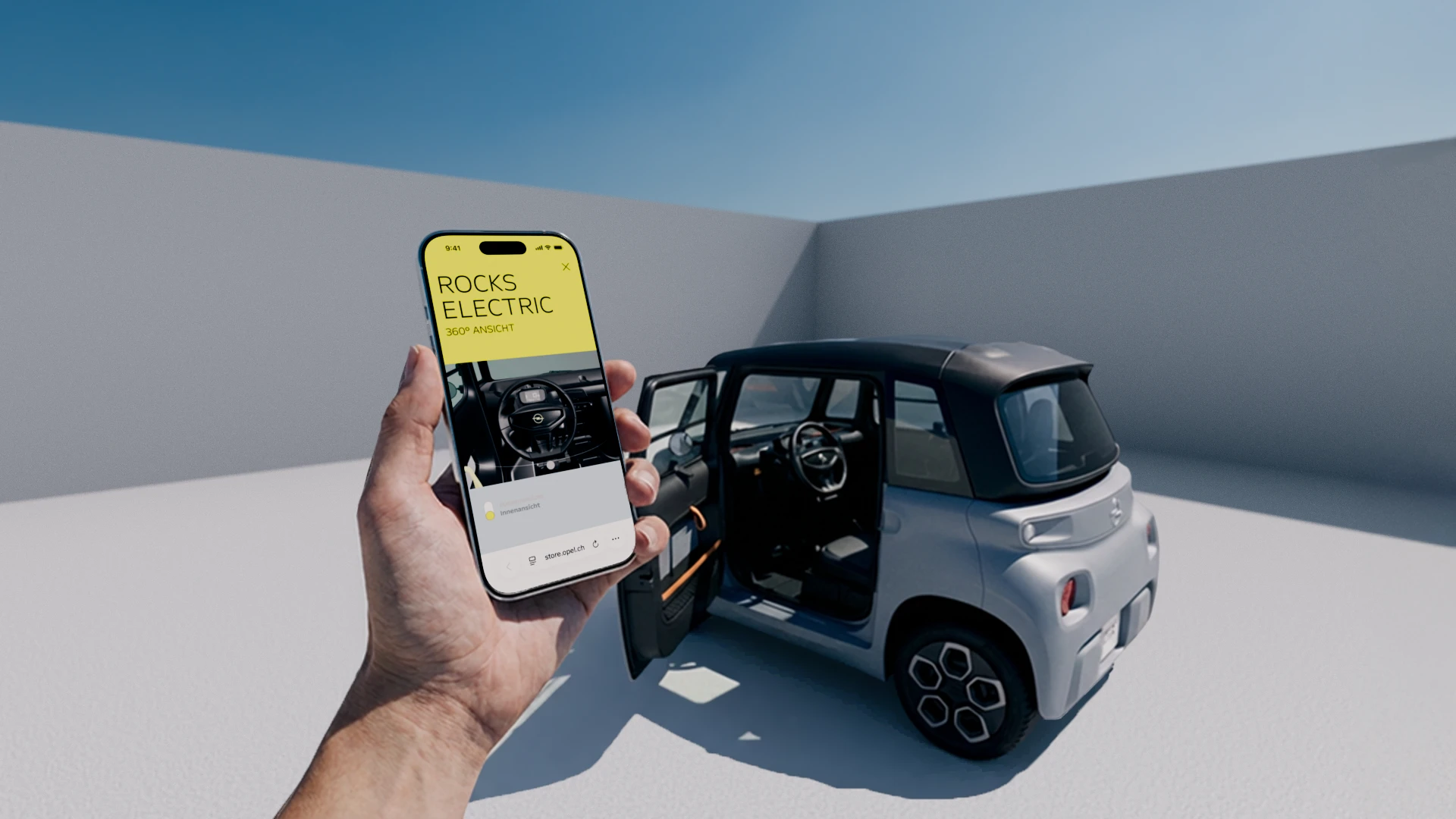 Eine Hand hält ein Smartphone, auf dem der Schweizer Online-Shop für den Opel Rocks Electric zu sehen ist. Dahinter steht das Auto mit offener Tur.
