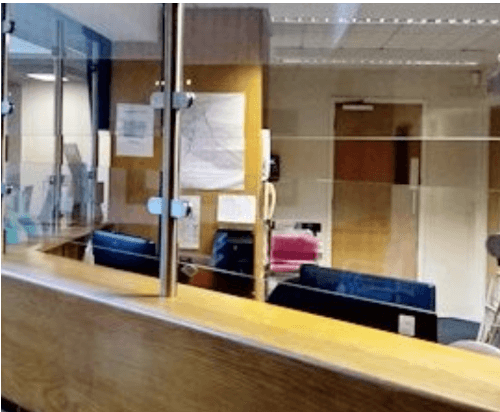 Image of the empty front desk at a facility, showcasing a glass barricade that is easy to reach through.