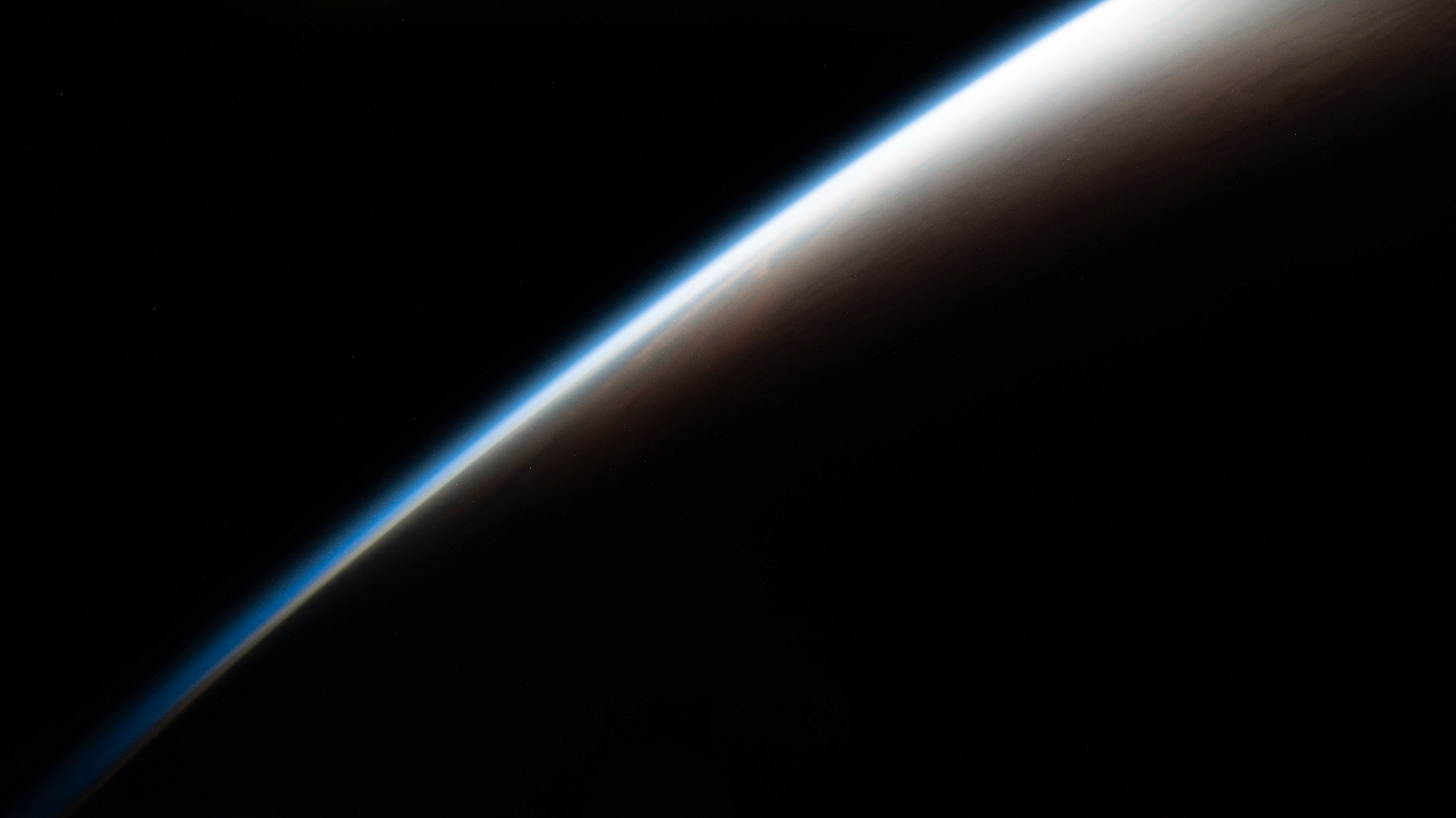 NASA photograph of Earth’s atmospheric horizon viewed from space, featuring a glowing blue atmospheric edge fading into darkness against the blackness of space.