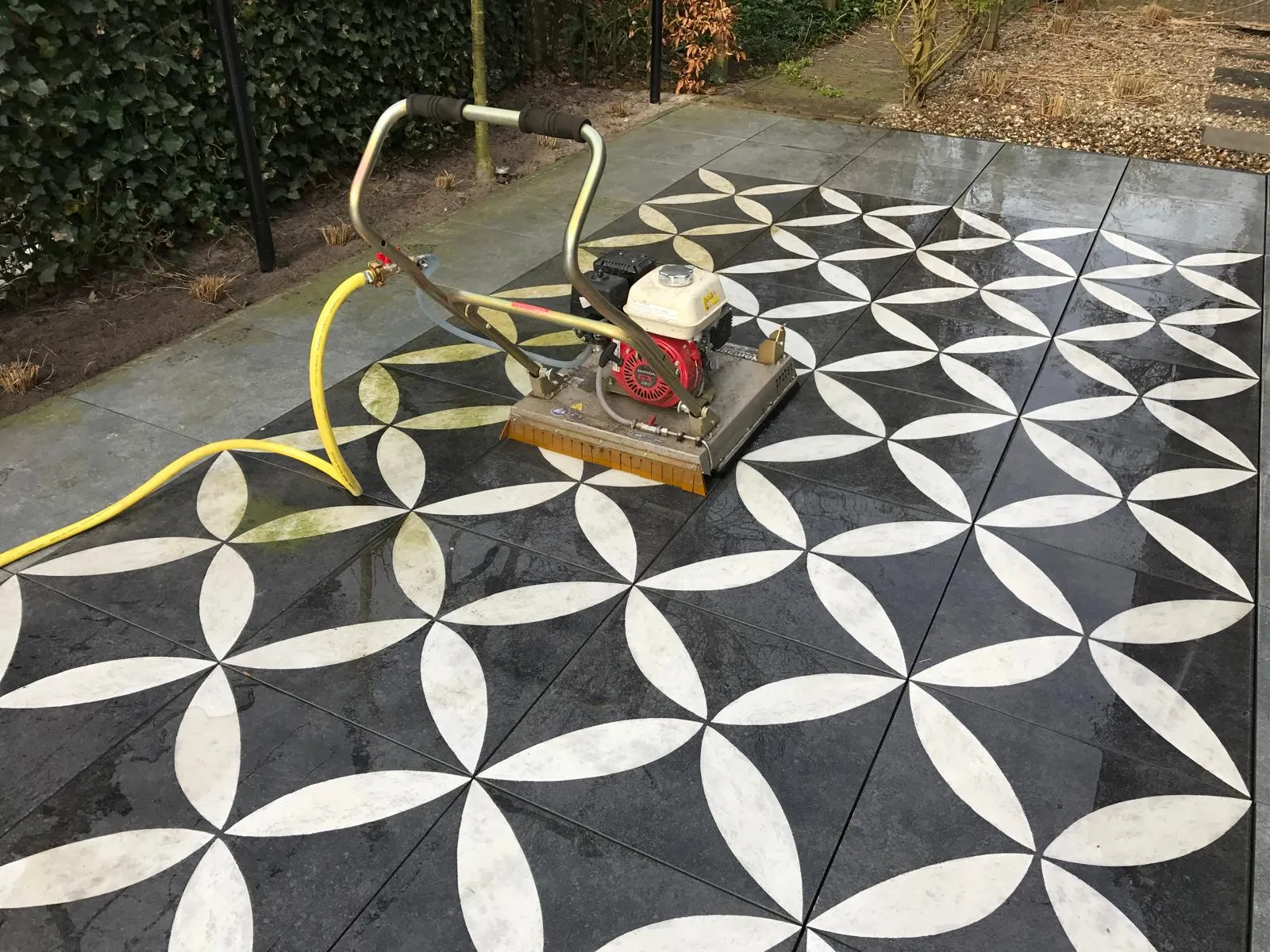 Reiniging van sierbestrating met trilplaat en slang tijdens onderhoud van terras in Gorredijk