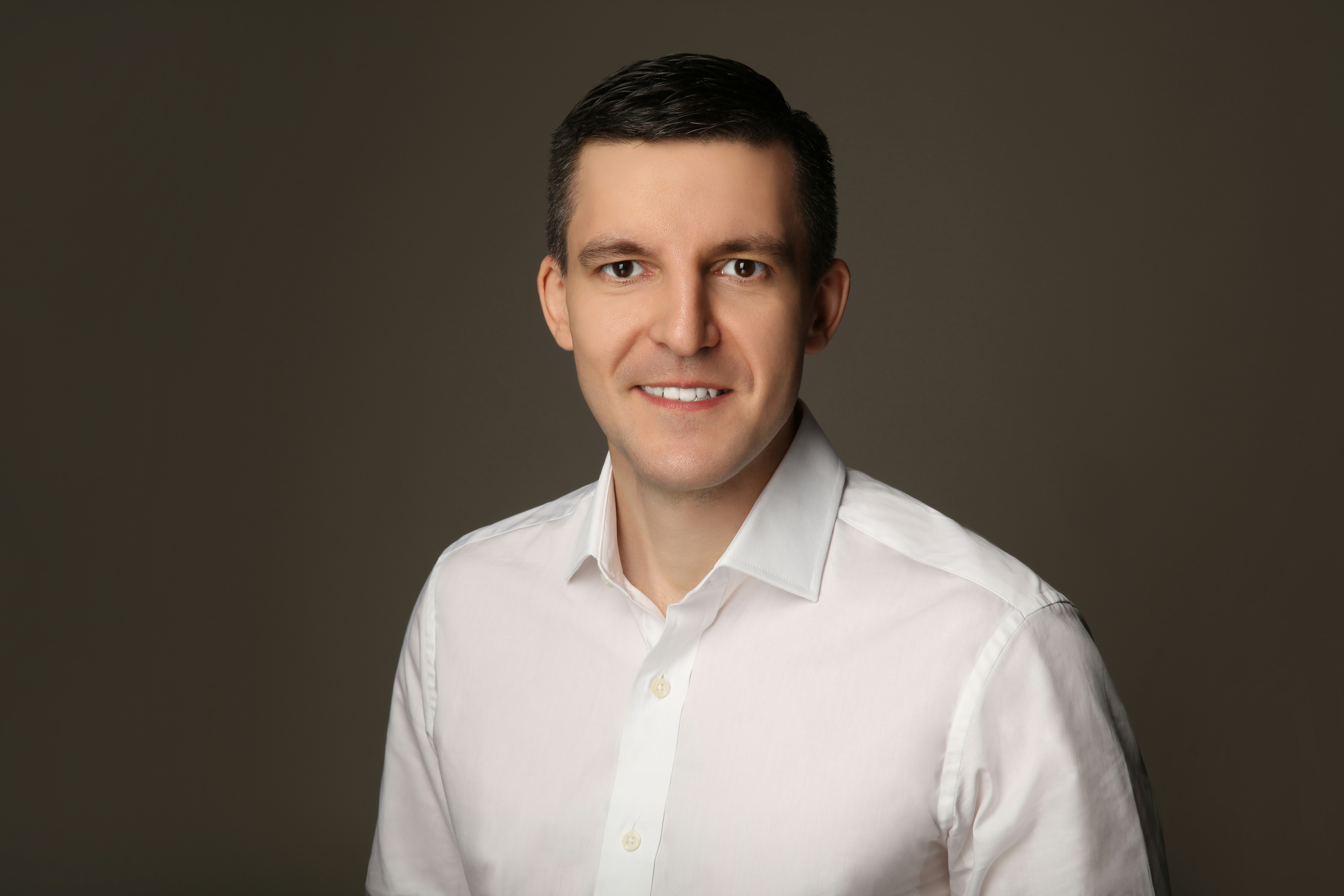 Man in white shirt smiling against a grey background