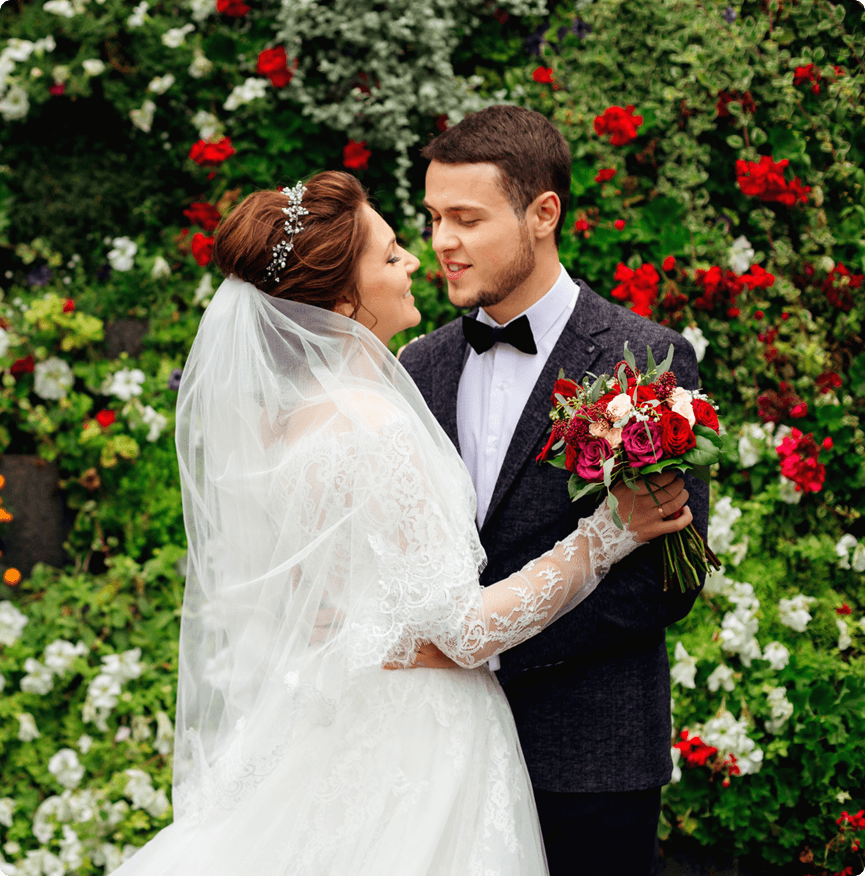 A joyful wedding scene with six people posing. The bride in a white gown and groom in a suit are surrounded by friends, colorful flowers, and autumn leaves. Everyone is smiling and making celebratory gestures.