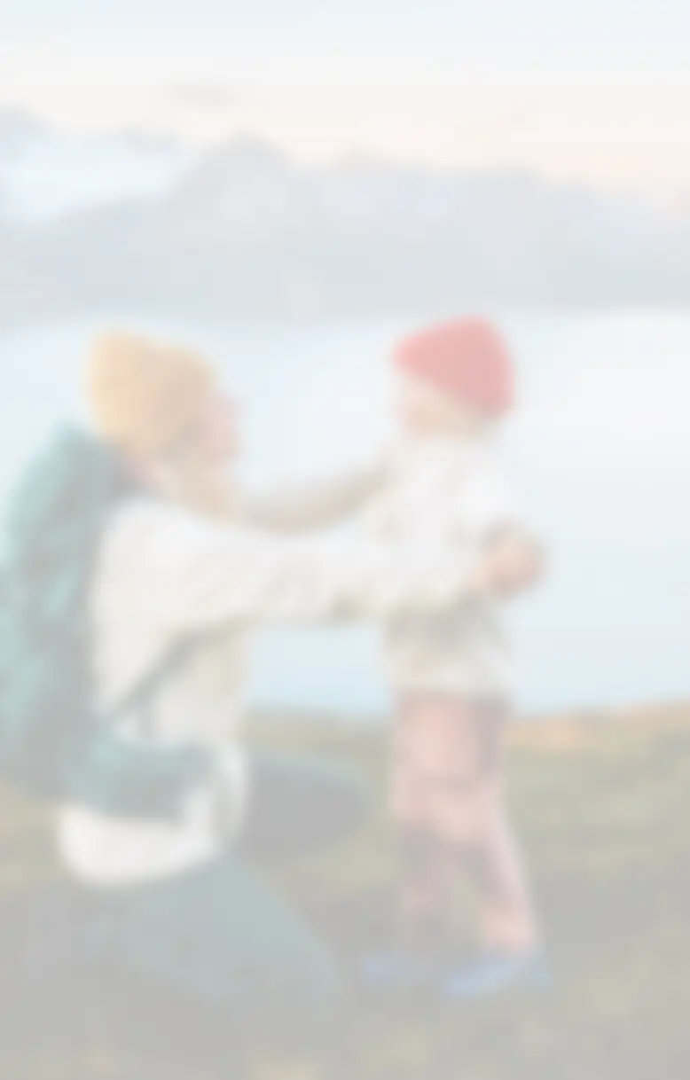 Mother and daughter outdoors, hiking near a large lake with mountains in the background.
